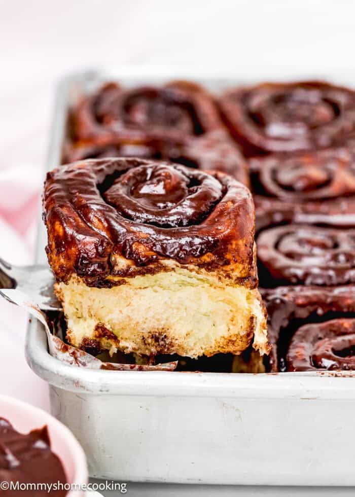 A tray of Eggless Chocolate Cinnamon Rolls with one roll being lifted out, exposing its soft, fluffy interior.