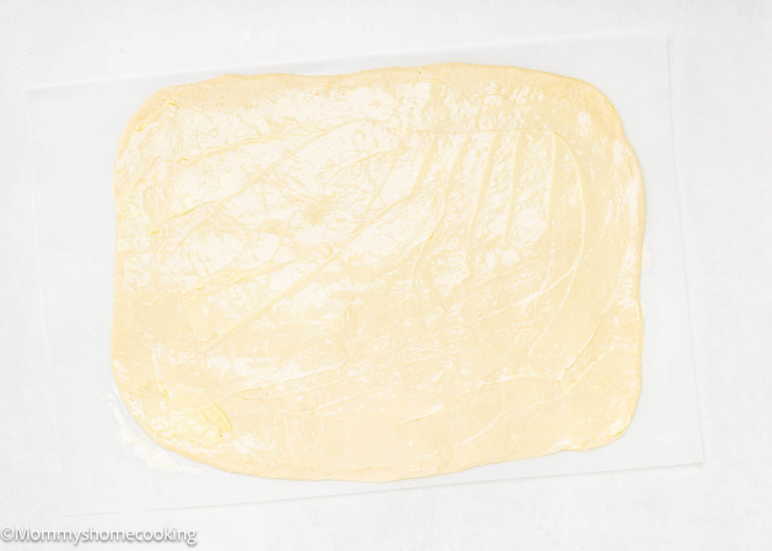 Rectangular sheet of raw dough rolled out thinly and placed on a piece of parchment paper, ready to be transformed into delicious Eggless Chocolate Cinnamon Rolls.