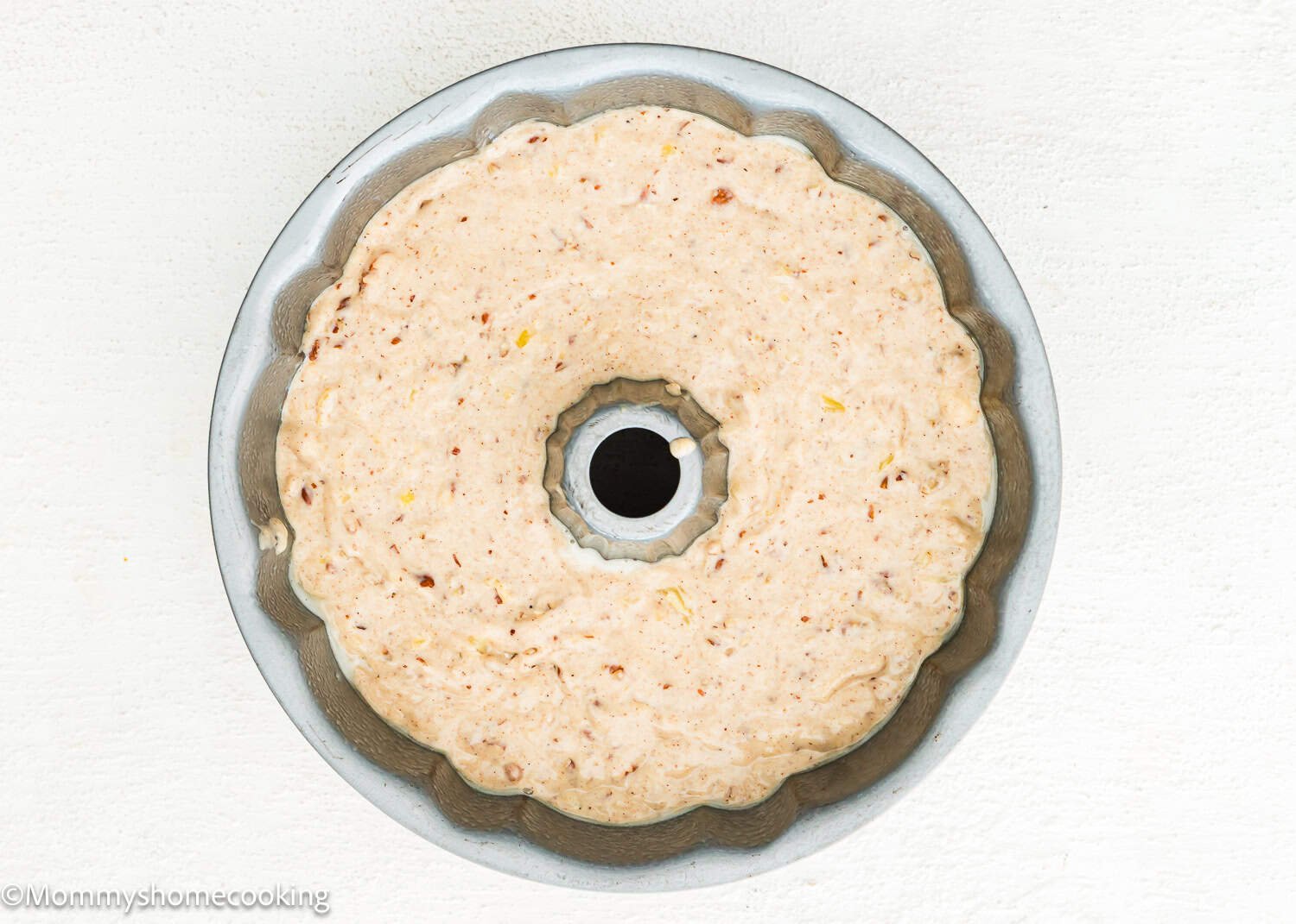 An Eggless Hummingbird Bundt Cake pan filled with unbaked cake batter, seen from above, on a white surface.