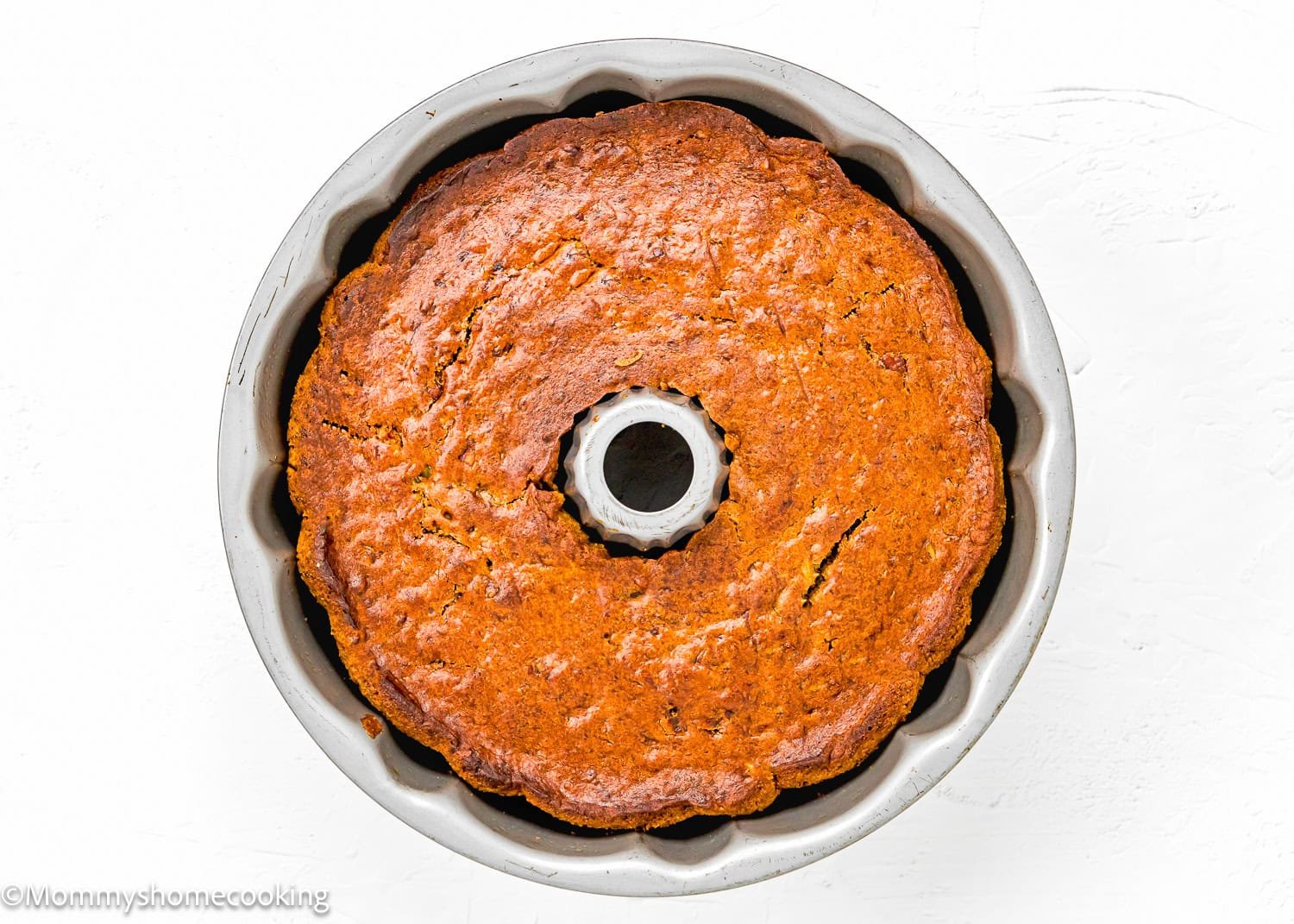 An baked Eggless Hummingbird Bundt Cake sits in a pan, viewed from above, on a white surface.
