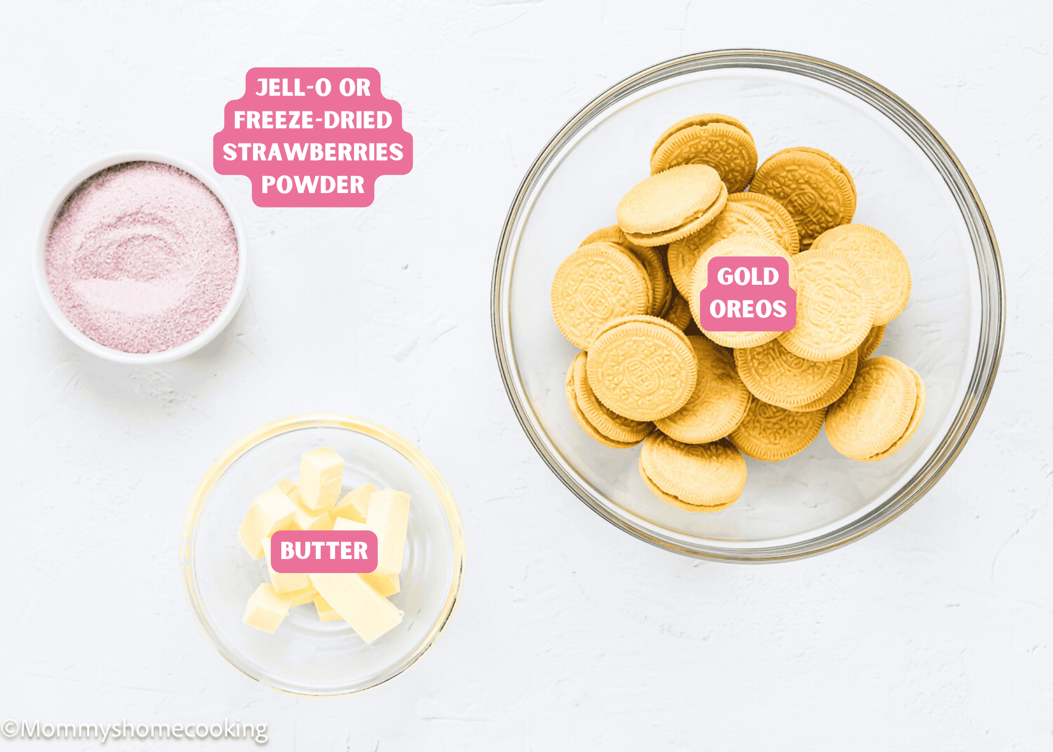 A bowl of Gold Oreos, a small bowl of butter slices, and a bowl of Jell-O or freeze-dried strawberries powder sit on a white surface—perfect for making an Eggless Strawberry Crunch Cake.