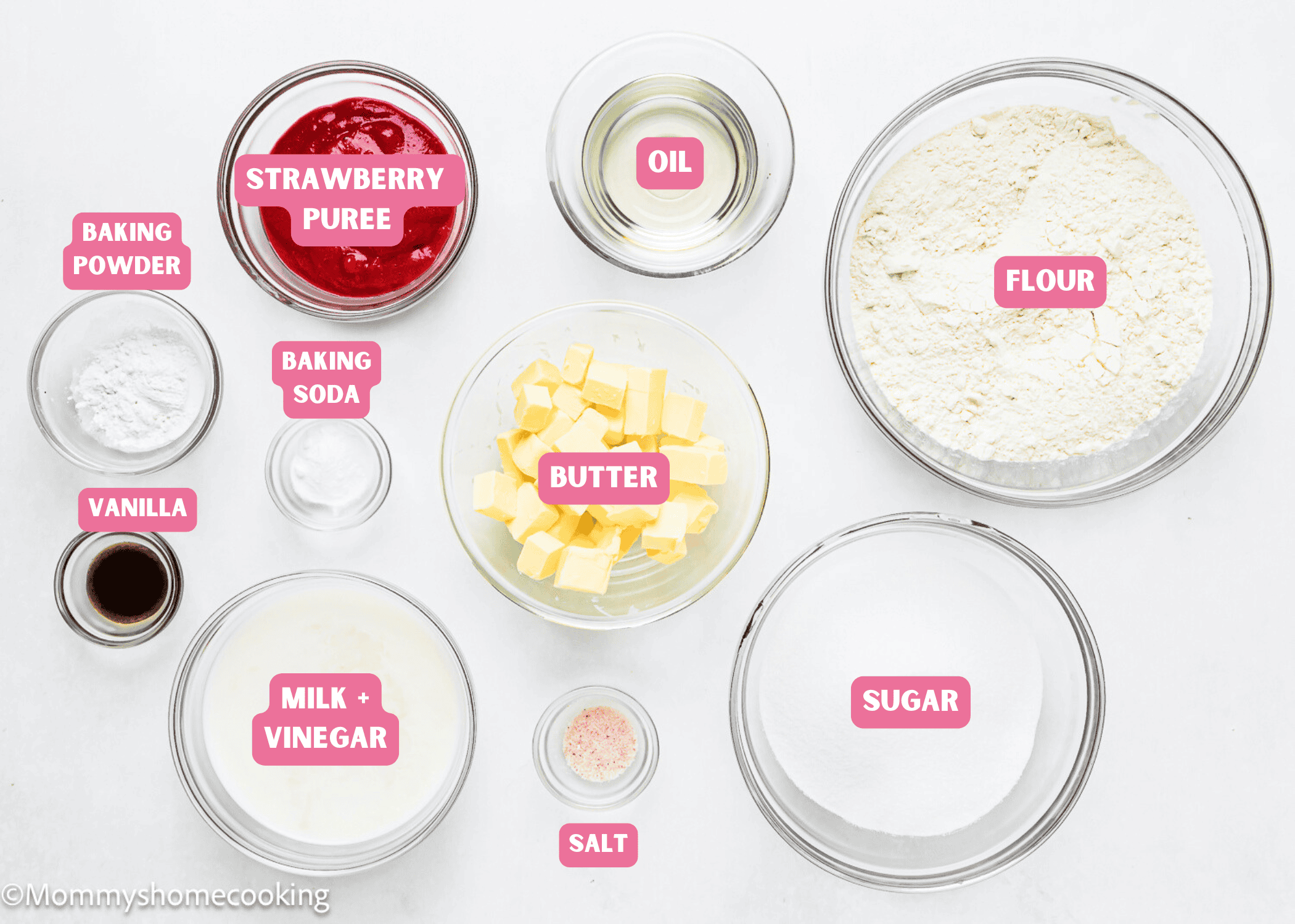 Various baking ingredients in bowls, including strawberry puree, oil, flour, butter, sugar, salt, milk with vinegar, vanilla, baking powder, and baking soda—perfect for making an Eggless Strawberry Crunch Cake—arranged on a white surface.