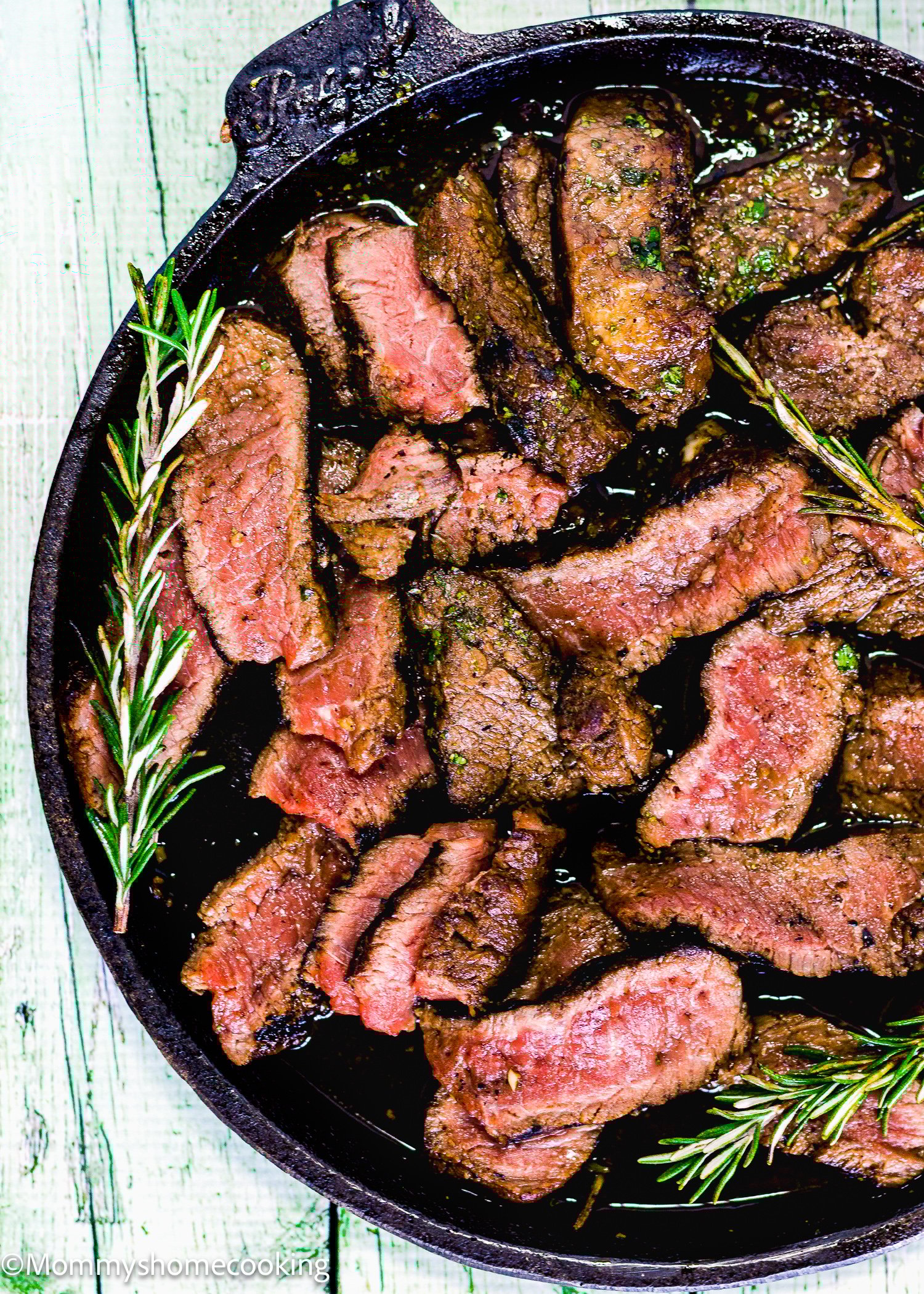 Grilled Balsamic Garlic Steak sliced and arranged in a cast iron skillet, garnished with sprigs of fresh rosemary.