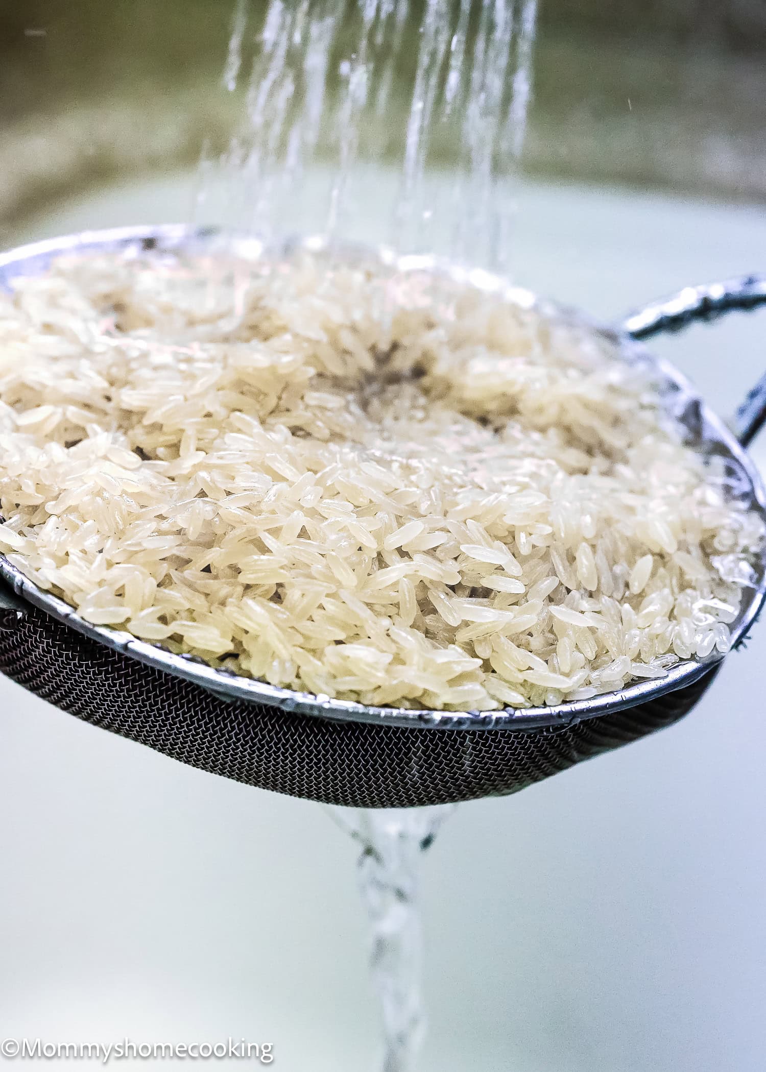 Uncooked rice being rinsed in a fine mesh strainer under running water—a crucial beginner-friendly guide step for making fluffy rice before you cook rice on the stove.