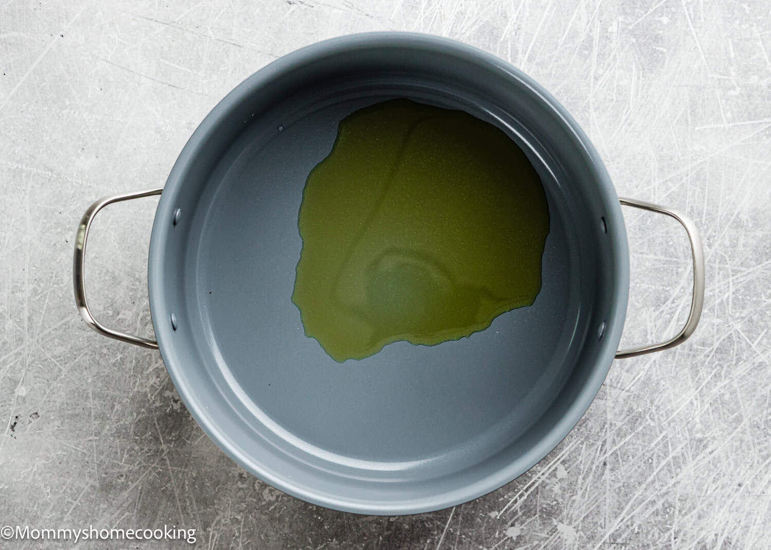 A large gray pot with metal handles containing a small amount of olive oil sits on a textured gray surface, perfect for learning How To Cook Fluffy Rice On Stove (Beginner-Friendly Guide!).