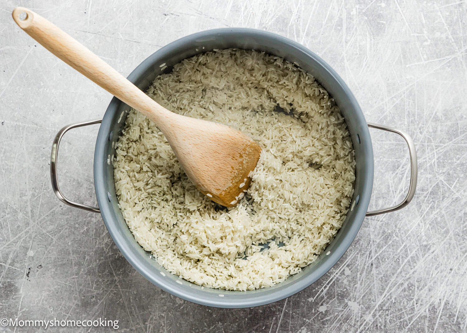 A pot filled with uncooked white rice and water, with a wooden spoon resting inside—perfect for anyone learning How To Cook Fluffy Rice On Stove (Beginner-Friendly Guide!).