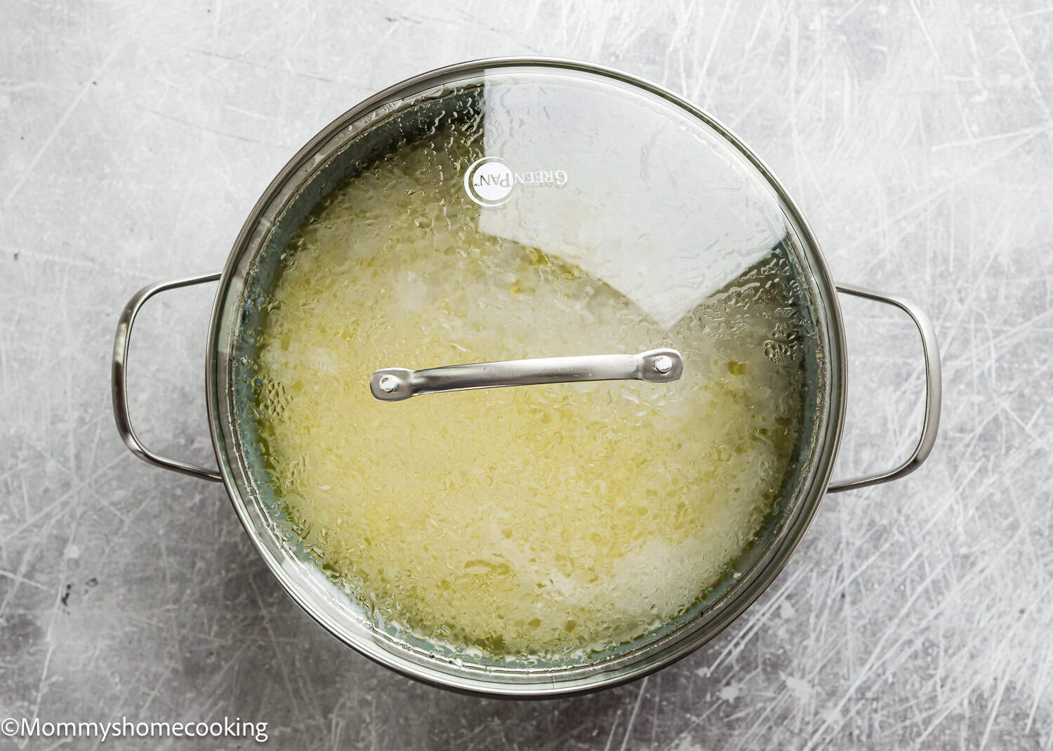 A pot of rice cooking with a glass lid, condensation visible, on a gray countertop. How To Cook Fluffy Rice On Stove (Beginner-Friendly Guide!).