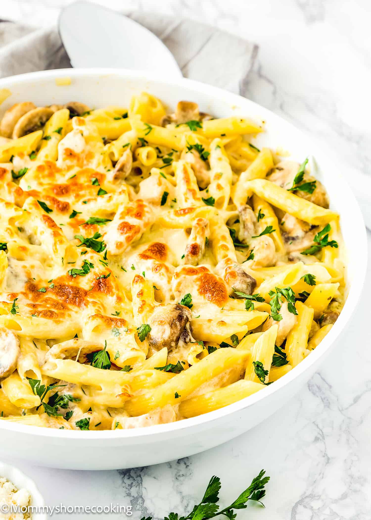 A white dish of one-pot easy chicken tetrazzini featuring baked penne pasta with creamy sauce, mushrooms, and a parsley garnish, all on a marble surface.