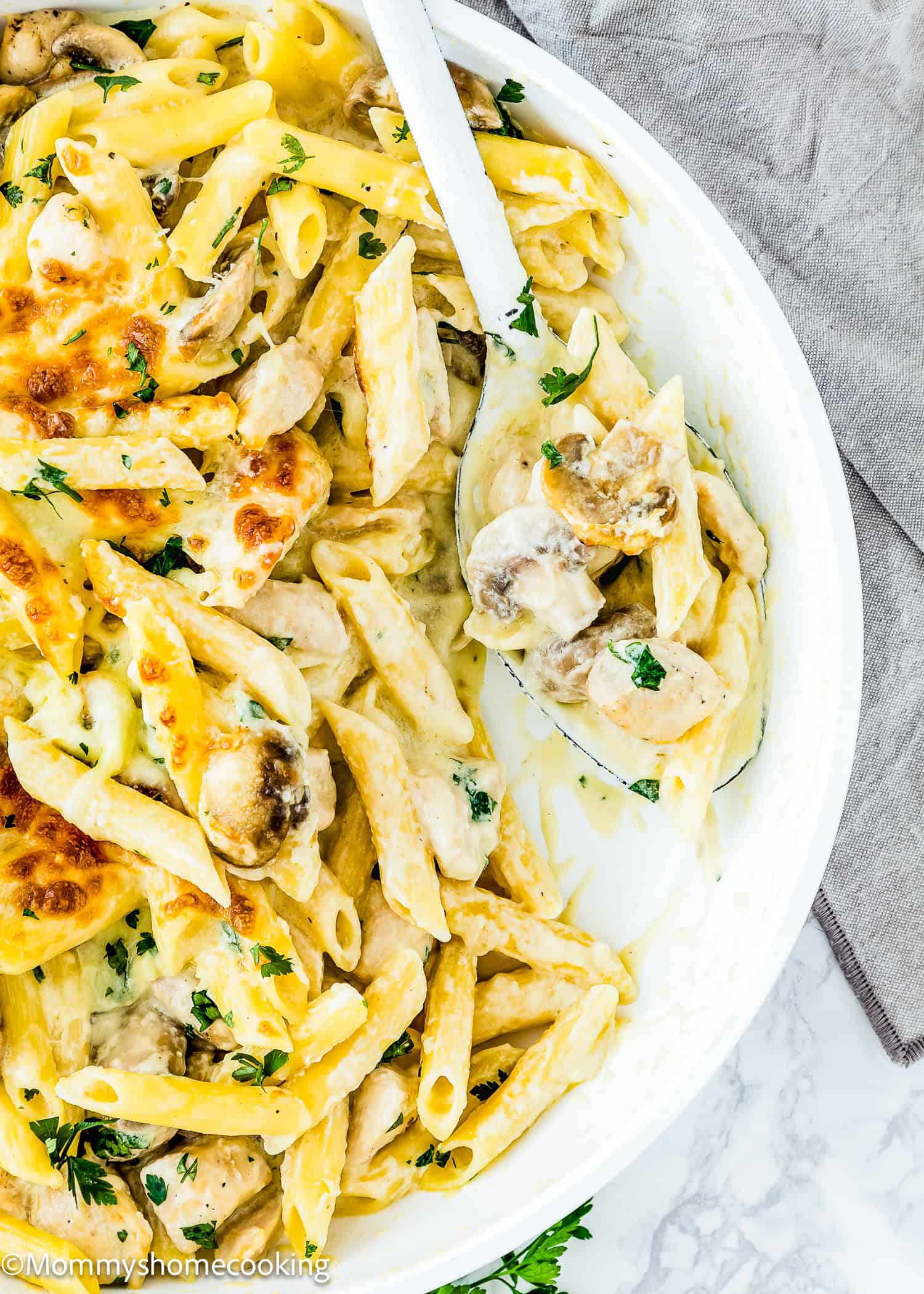 One-Pot Easy Chicken Tetrazzini: Creamy pasta with chicken and mushrooms topped with melted cheese and parsley, all in a white dish accompanied by a serving spoon.