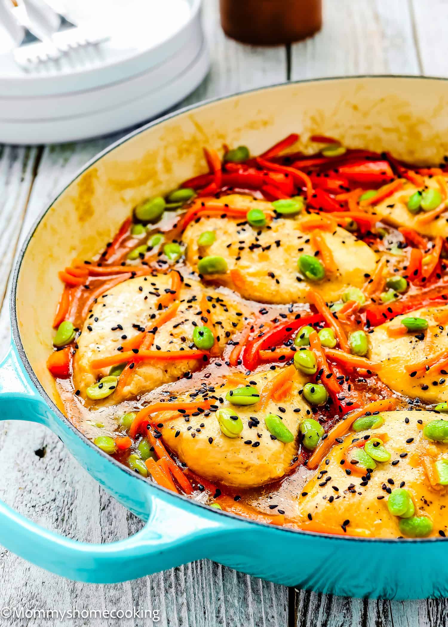 Orange Ginger Chicken breast pieces cooked with sliced red bell peppers, carrots, green onions, and black sesame seeds in a light sauce, served in a blue skillet on a wooden surface.