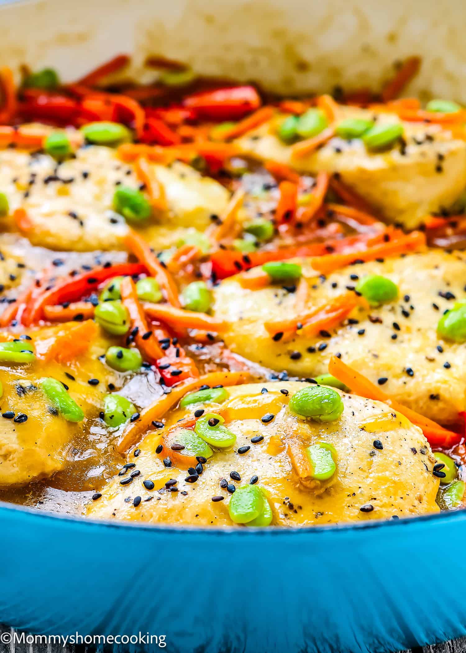 Orange Ginger Chicken breasts in sauce, garnished with black sesame seeds, sliced green onions, and julienned carrots, cooked in a blue pan.