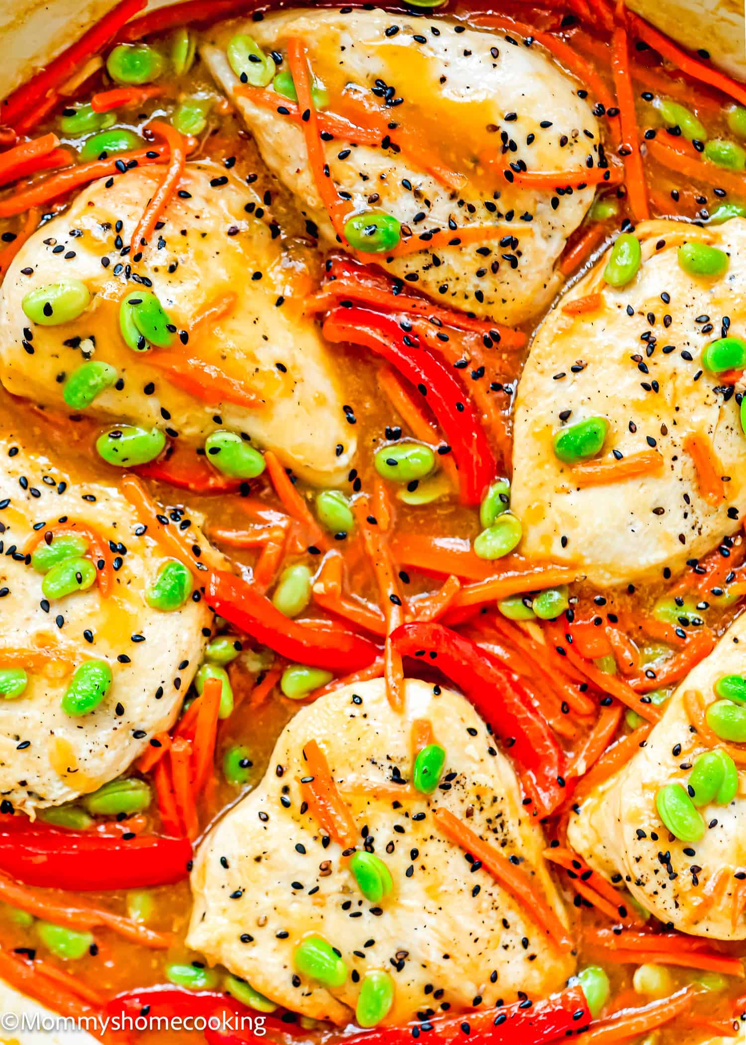 Orange Ginger Chicken breasts cooked in a creamy orange sauce with sliced red bell peppers, shredded carrots, edamame, and black sesame seeds, viewed from above.