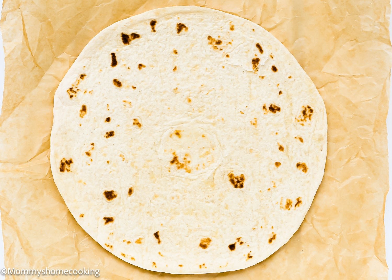 A plain flour tortilla on a sheet of brown parchment paper, ready to become a base for Super Easy Pizzadillas.