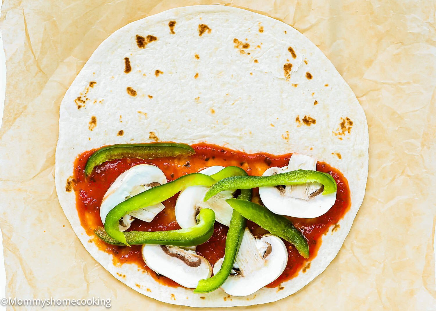 A flour tortilla topped with tomato sauce, sliced mushrooms, and green bell pepper strips on parchment paper—Super Easy Pizzadillas for a quick meal.