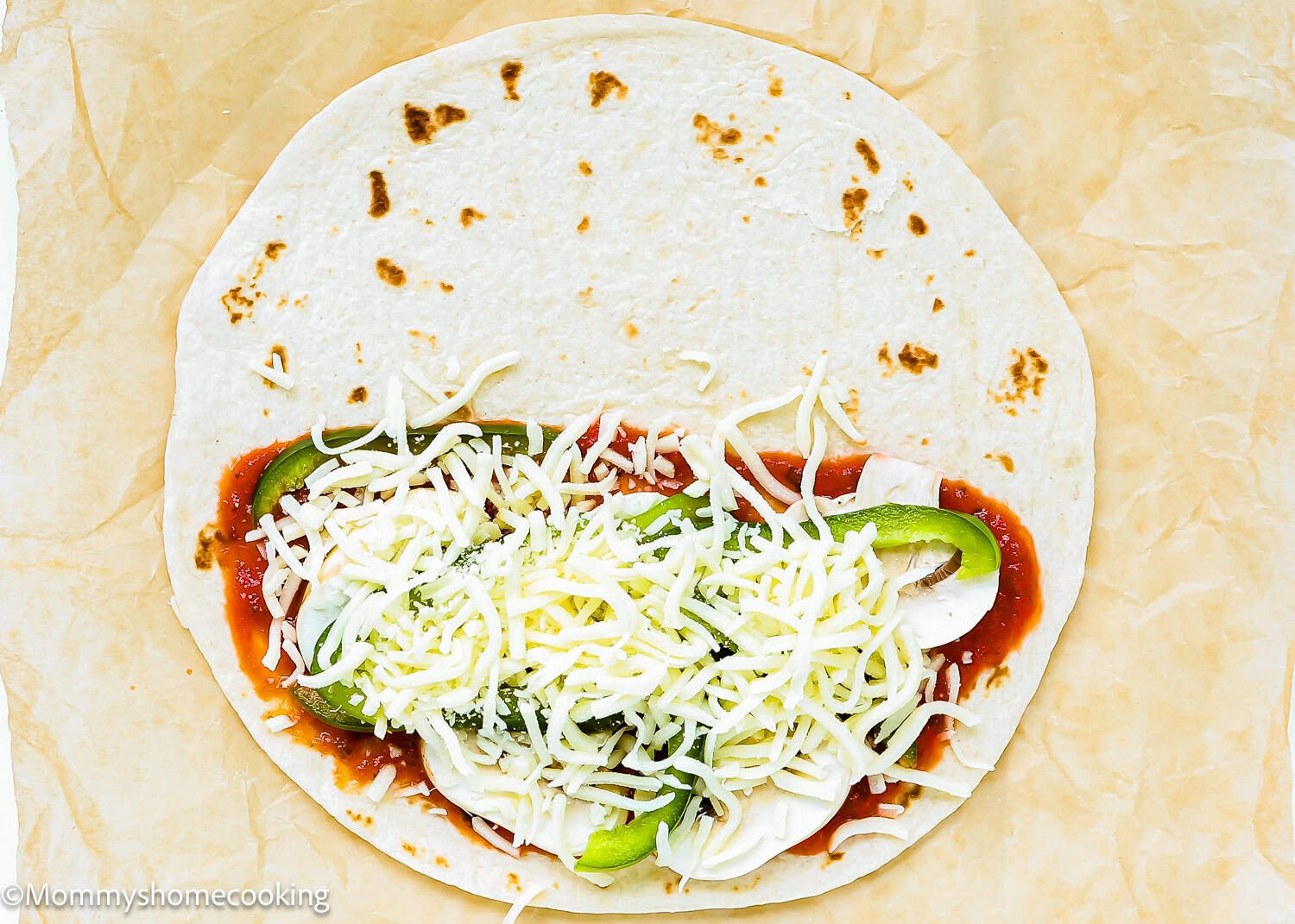 A flour tortilla topped with tomato sauce, sliced green bell peppers, mozzarella cheese, and mushrooms on parchment paper makes Super Easy Pizzadillas.