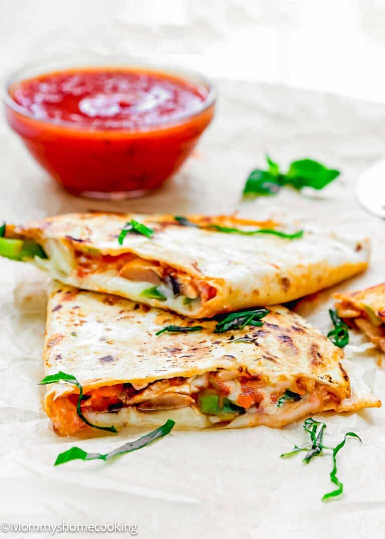 Two cheesy vegetable quesadillas, also known as Super Easy Pizzadillas, are cut in half and served on parchment paper, garnished with fresh herbs, with a bowl of red salsa in the background.