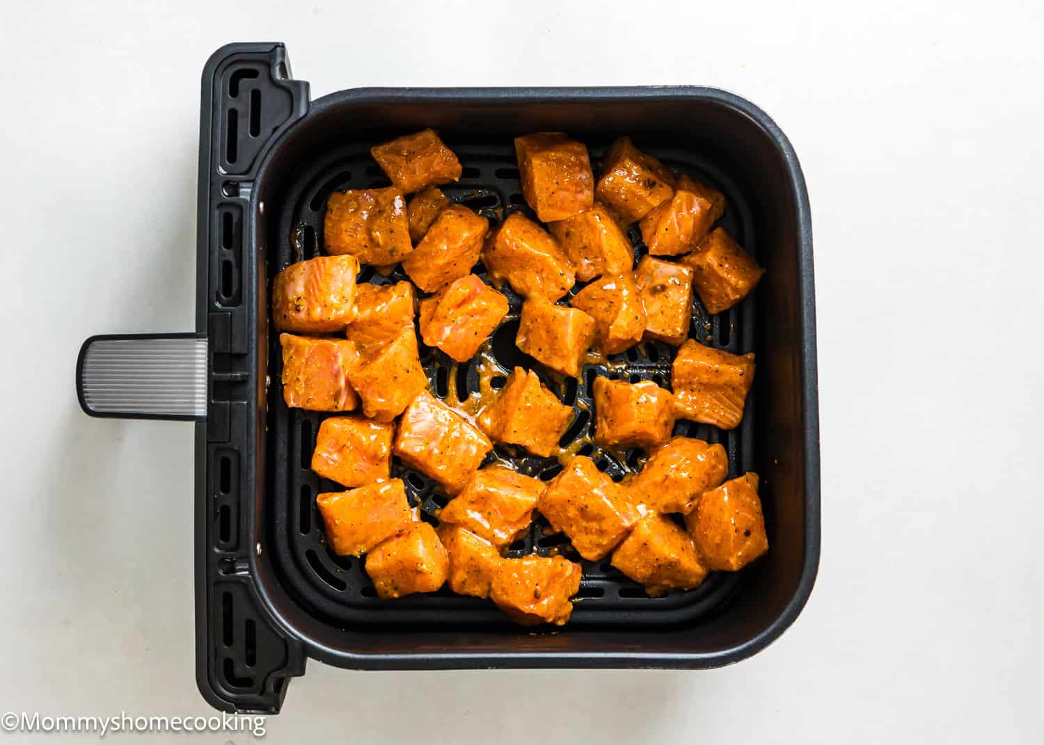 Easy Air Fryer Salmon Bites: Cubed, seasoned pieces of salmon arranged in a single layer inside an air fryer basket, ready to be cooked.