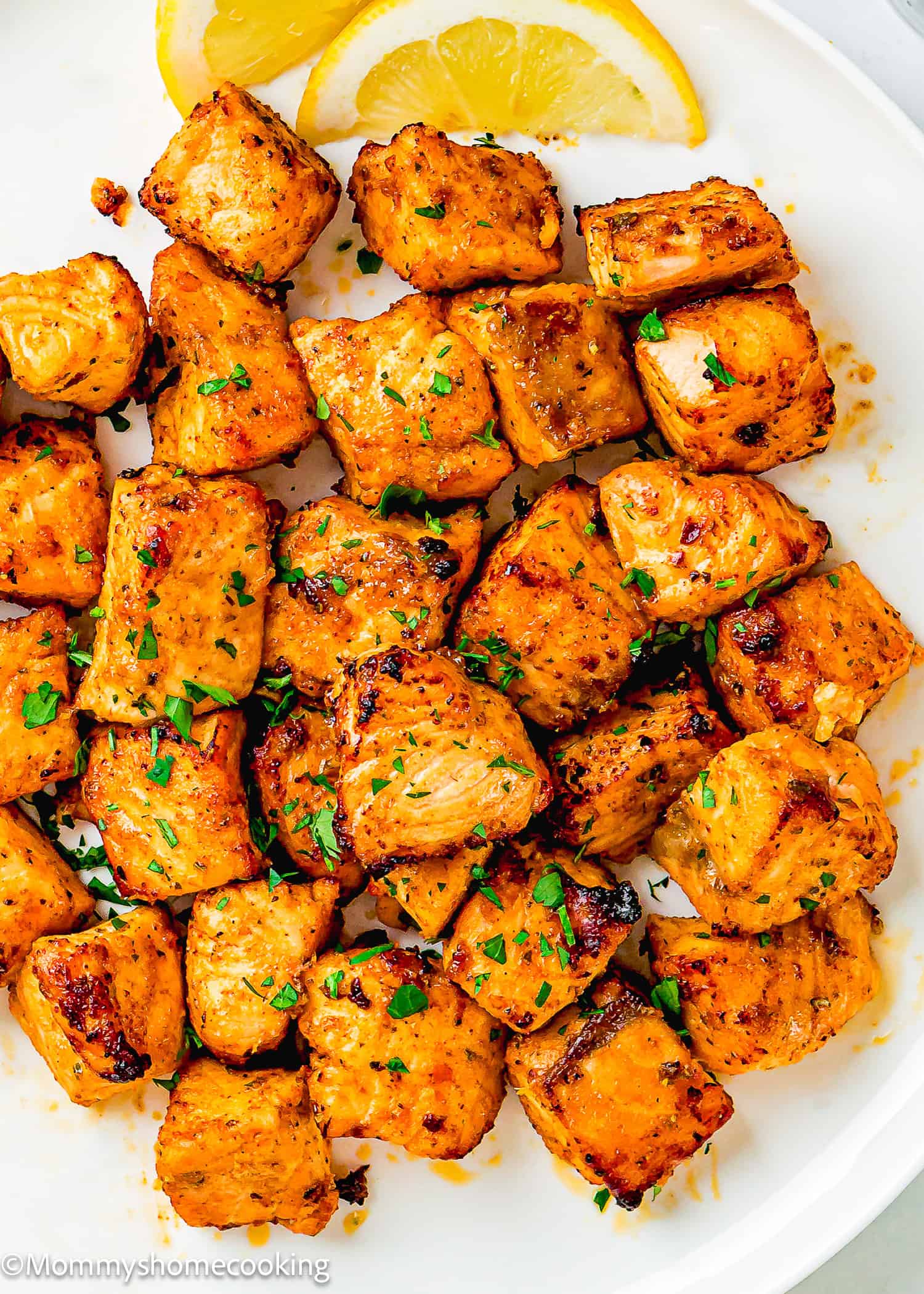 Grilled, seasoned chicken cubes garnished with chopped herbs and lemon wedges, served on a white plate—perfect alongside Easy Air Fryer Salmon Bites.