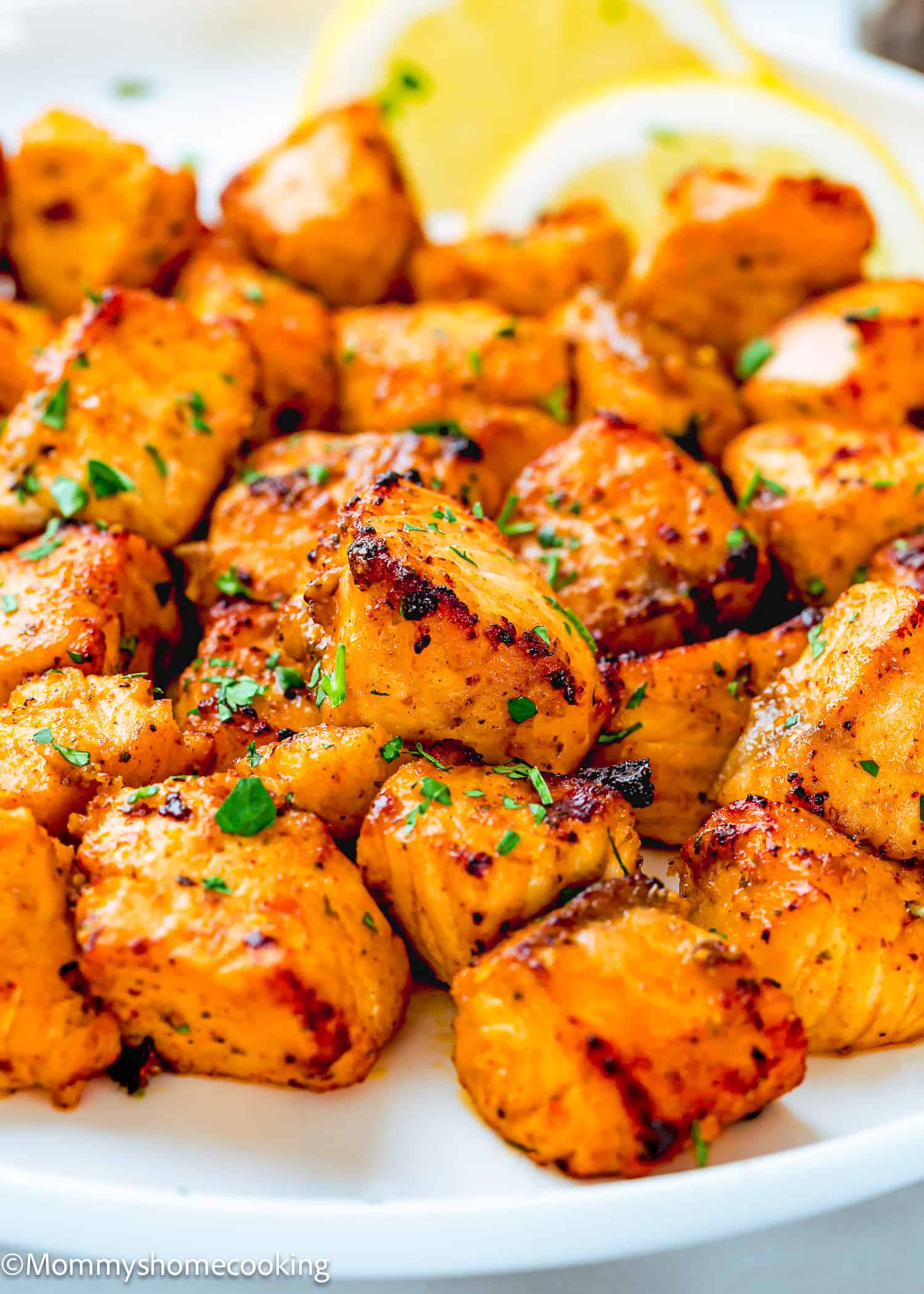 Close-up of grilled, seasoned chicken pieces garnished with chopped herbs, served on a white plate with lemon slices in the background—perfect alongside Easy Air Fryer Salmon Bites.
