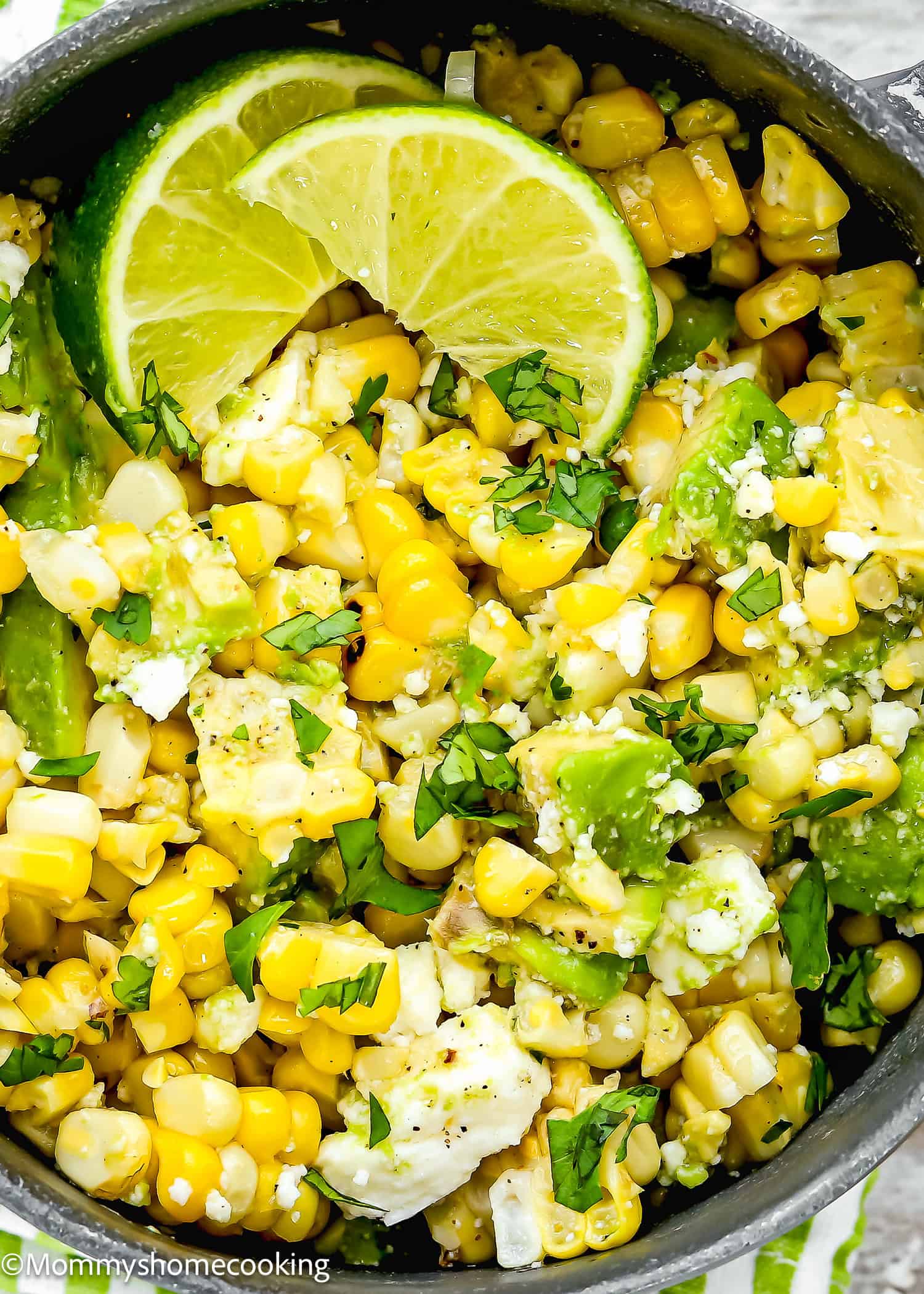 A close-up of Easy Avocado Corn Salad (No Mayo) with crumbled cheese, chopped cilantro, and two lime slices on top.