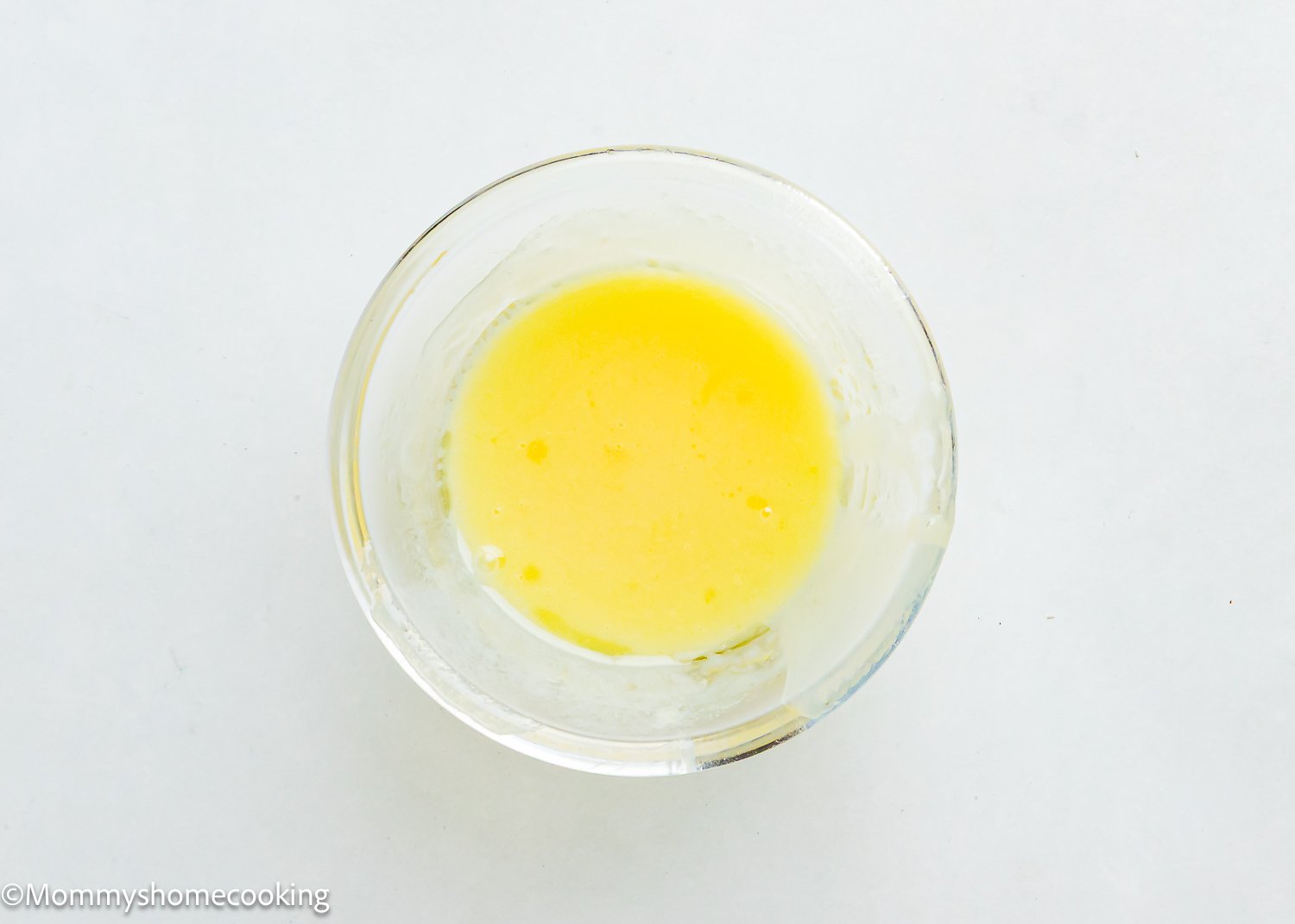 A clear glass bowl containing a mixture of melted butter and milk on a plain white surface, ready to be used in Eggless Chocolate Chip Brioche Rolls.