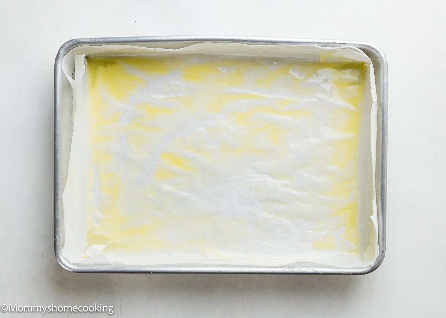 A rectangular baking pan lined with parchment paper and brushed with butter or oil, ready to bake Eggless Chocolate Chip Brioche Rolls, sits on a white surface.