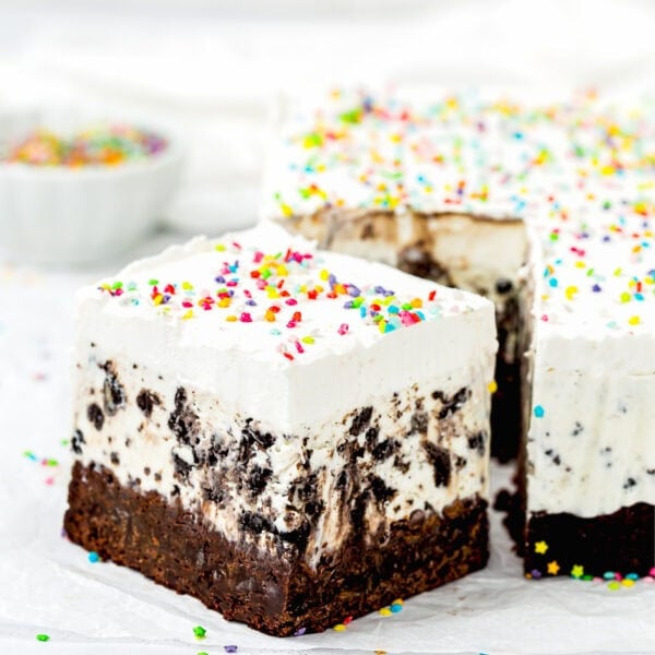 An Eggless Ice Cream Cake bar with a brownie base, cookies and cream ice cream layer, whipped topping, and colorful sprinkles, sliced and ready to serve.