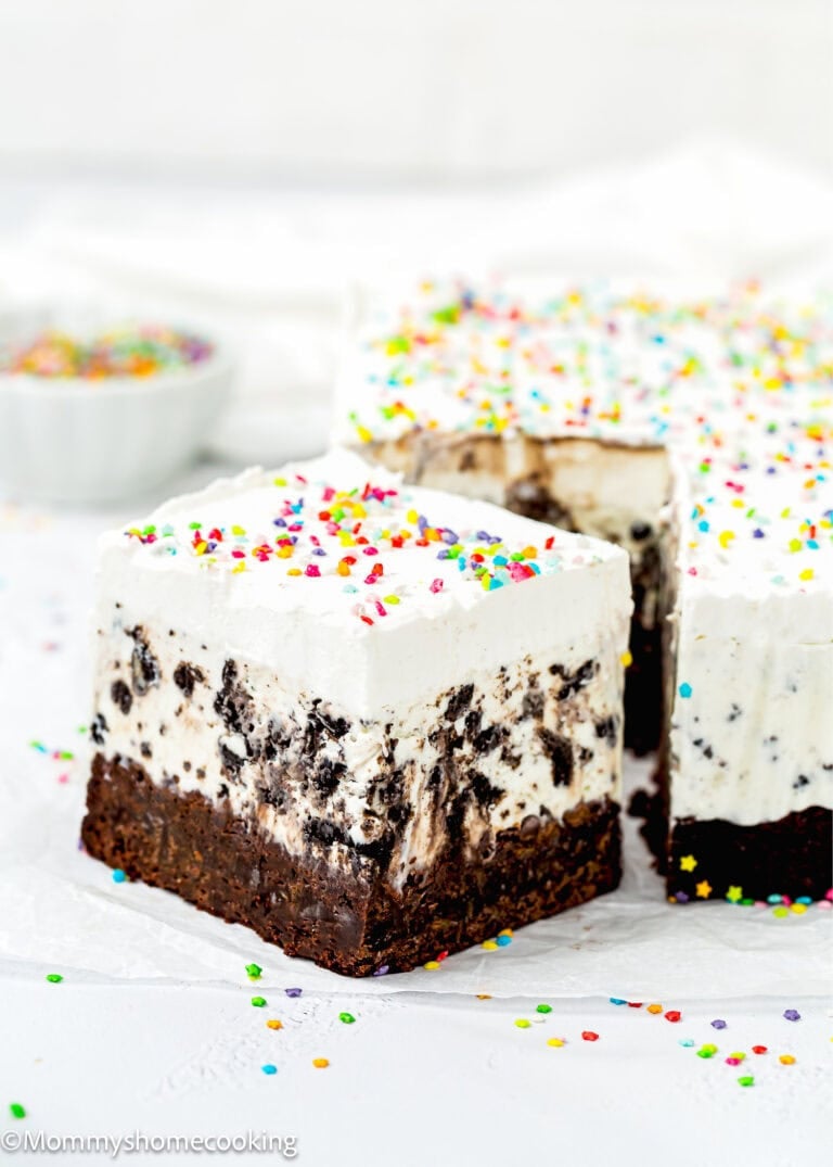 An Eggless Ice Cream Cake bar with a brownie base, cookies and cream ice cream layer, whipped topping, and colorful sprinkles, sliced and ready to serve.