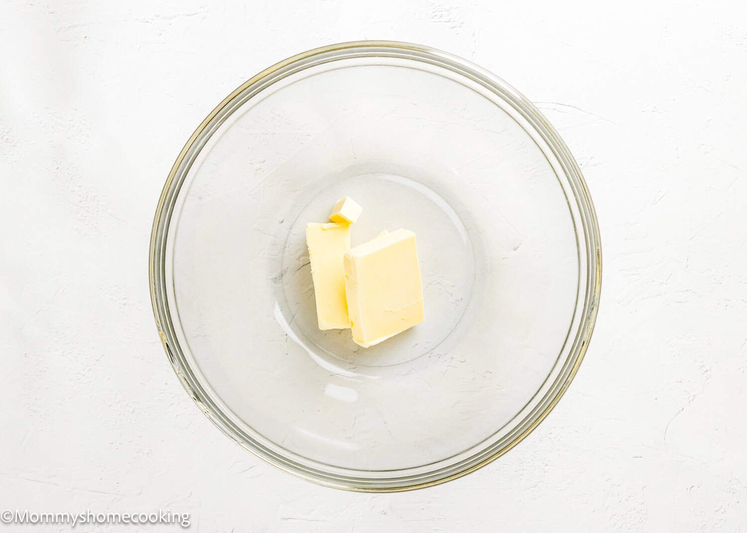 A large clear glass bowl with two pieces of butter inside, placed on a white surface—perfect for starting your Eggless Texas Sheet Cake.