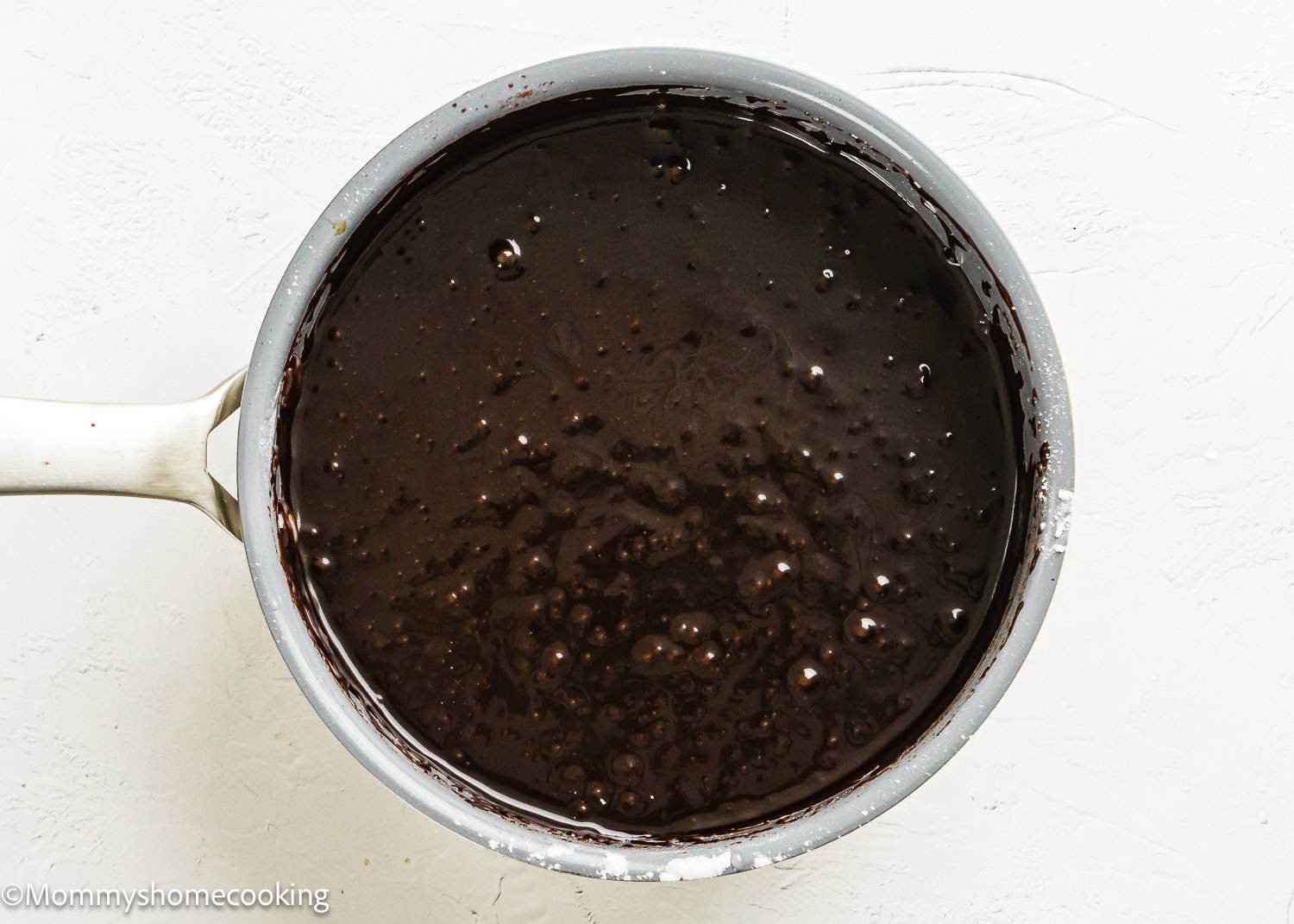 A saucepan filled with smooth, dark chocolate batter for Eggless Texas Sheet Cake sits on a white surface.