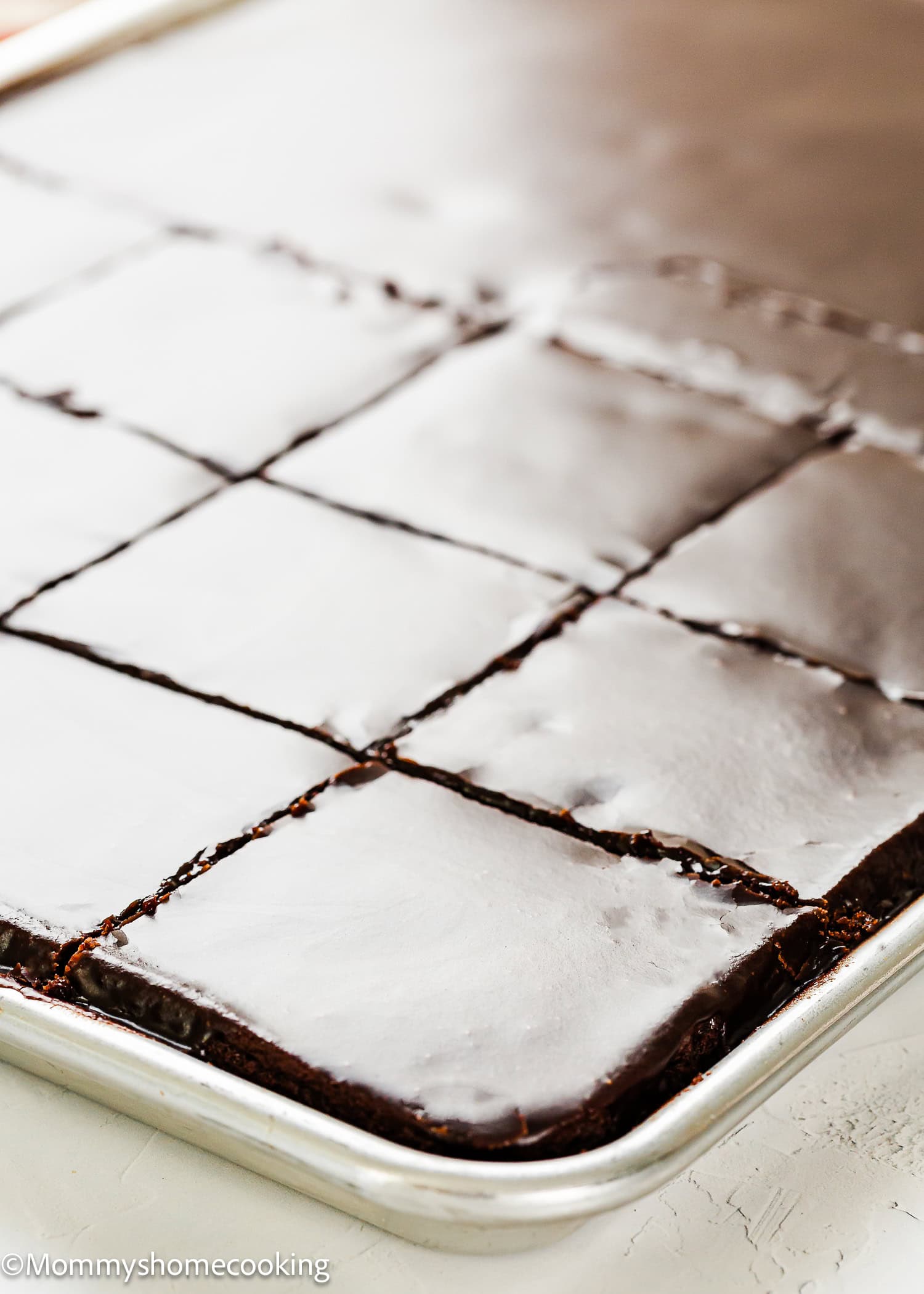 A sheet pan of Eggless Texas Sheet Cake cut into squares, topped with a smooth layer of chocolate icing.
