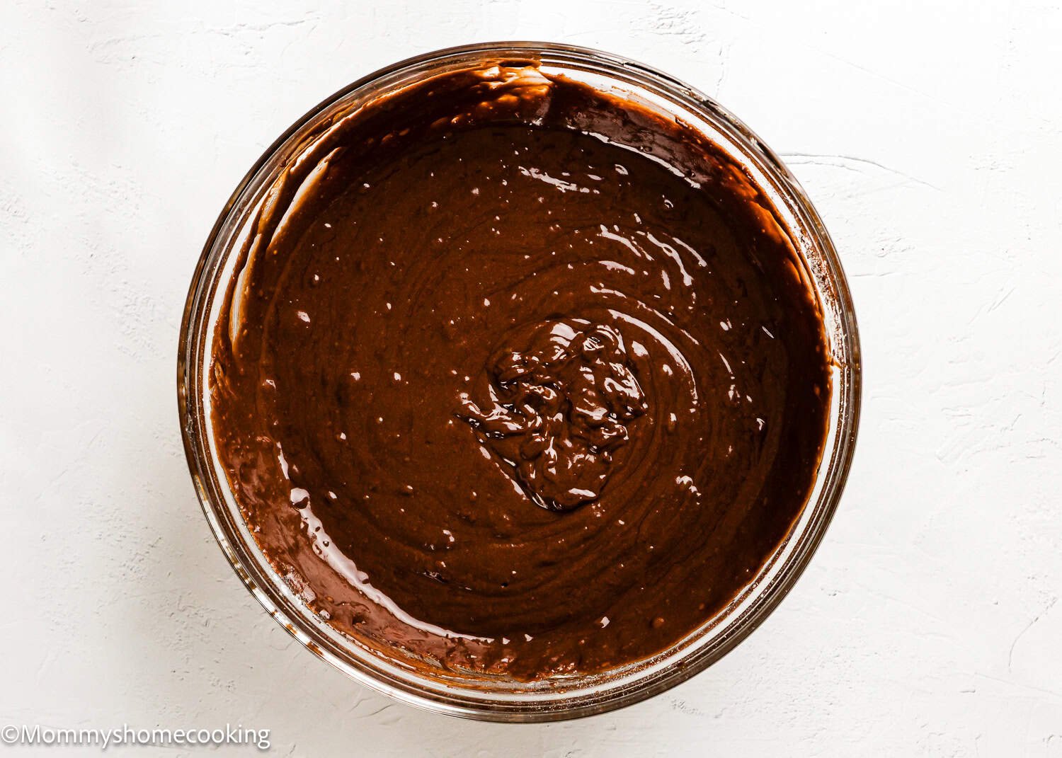 A glass bowl filled with Eggless Texas Sheet Cake batter, resting on a white surface.