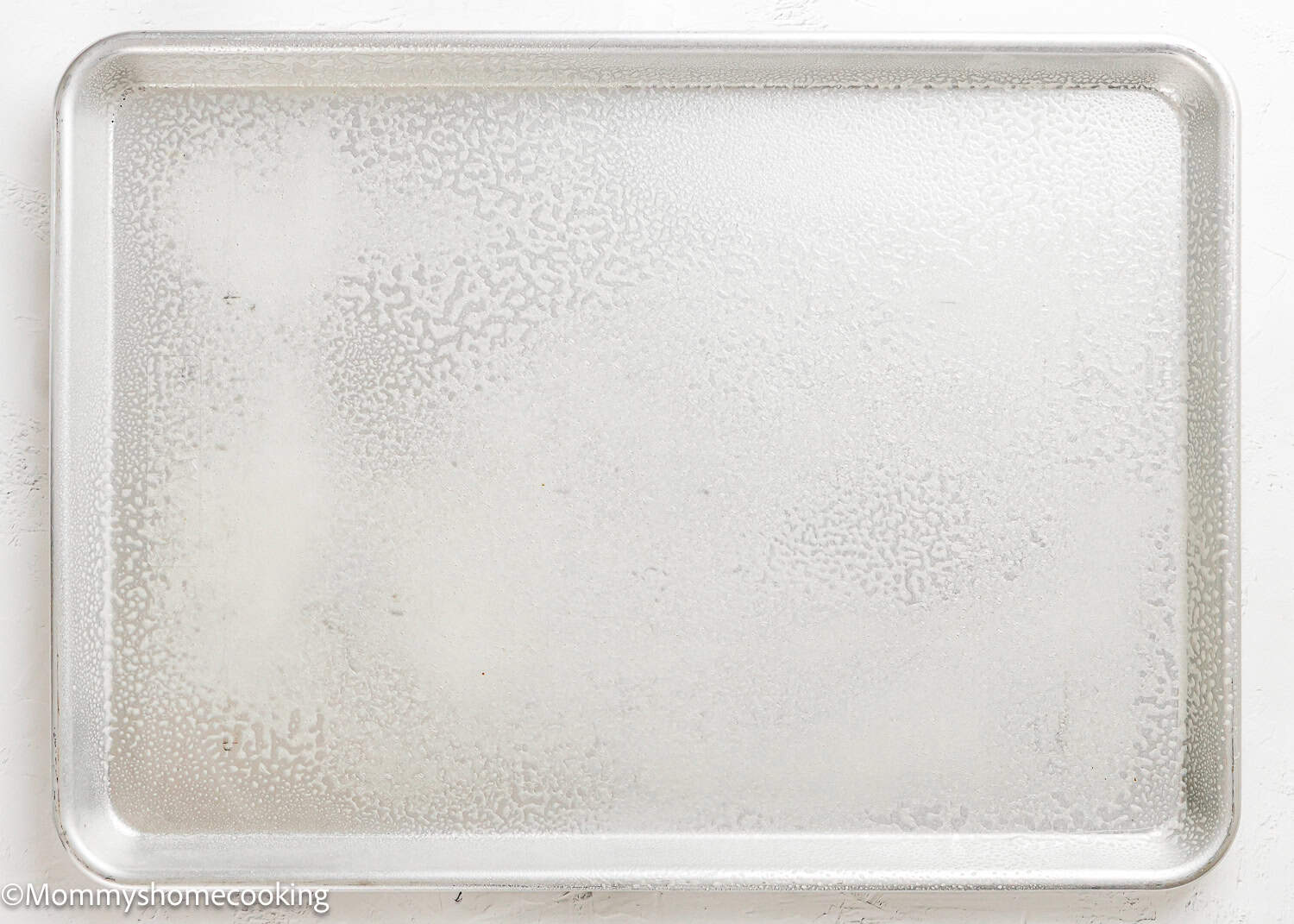 A silver baking sheet is lightly sprayed with oil, ready for preparing Eggless Texas Sheet Cake, and rests on a white surface.
