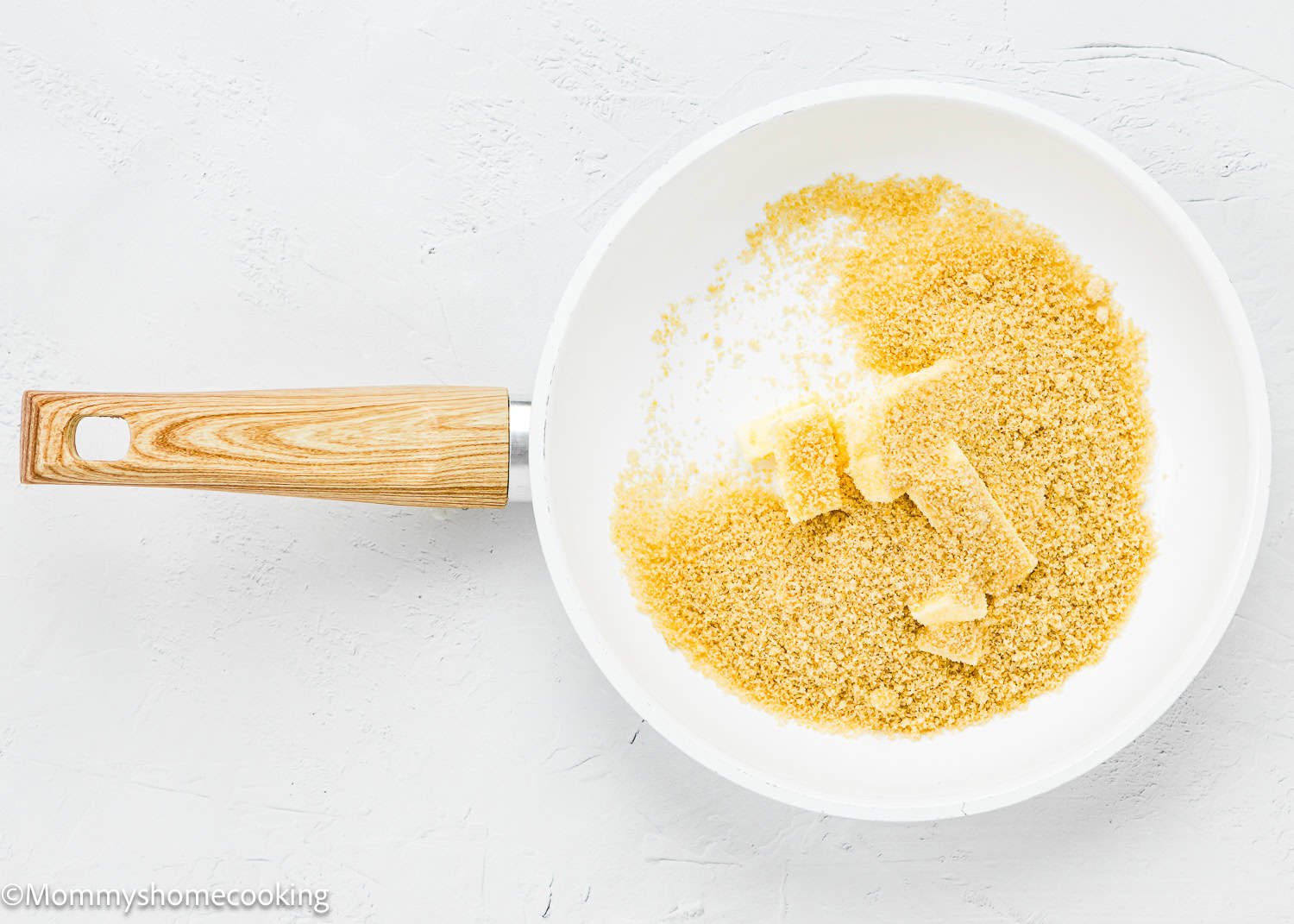A white pan with wooden handle contains brown sugar and chunks of butter on a light surface, perfect for making Eggless Upside-Down Peach Cake.