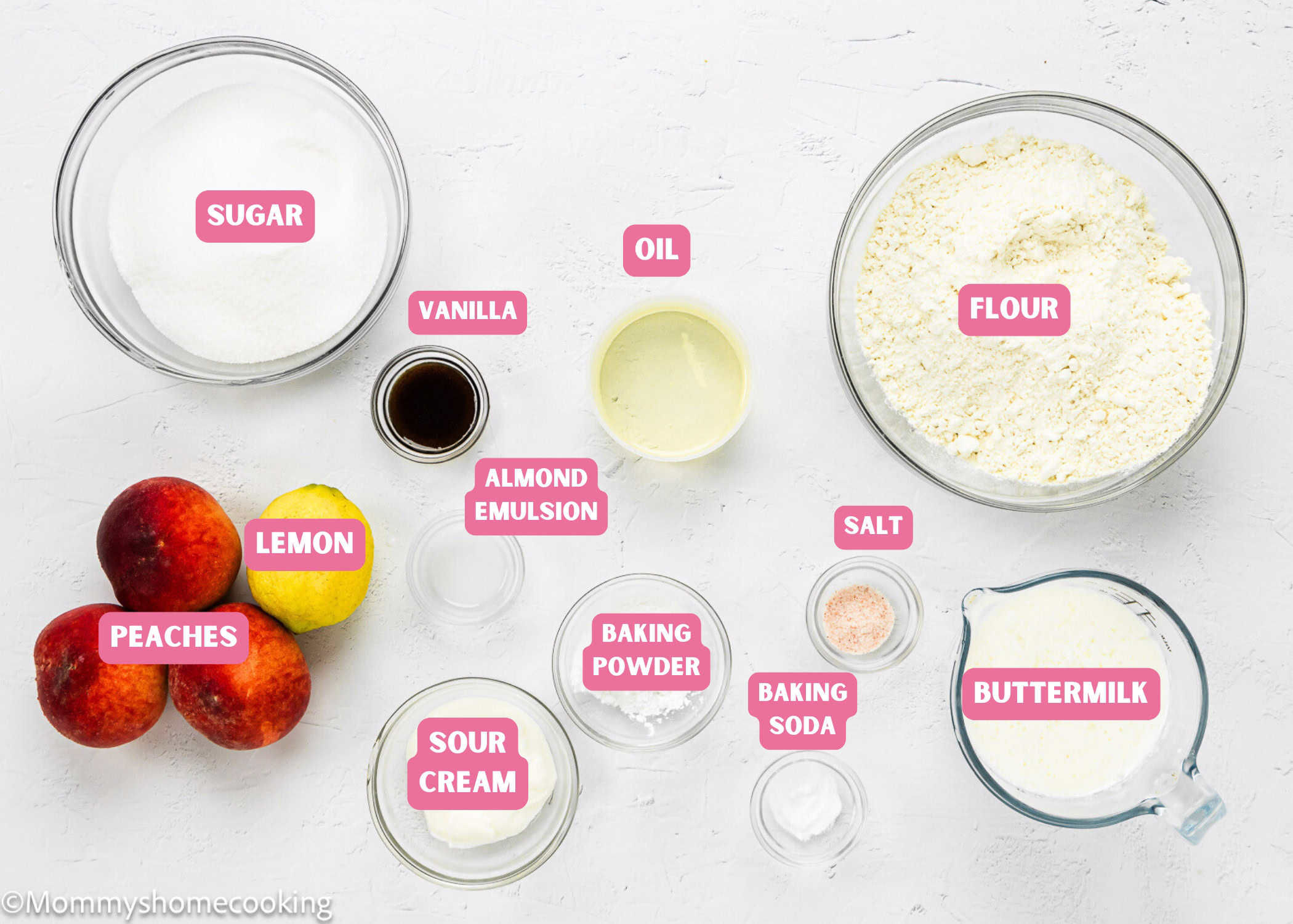 Top-down view of measured ingredients for Eggless Upside-Down Peach Cake in bowls and jars labeled sugar, vanilla, oil, flour, lemon, peaches, almond emulsion, sour cream, salt, buttermilk, baking powder, and baking soda.