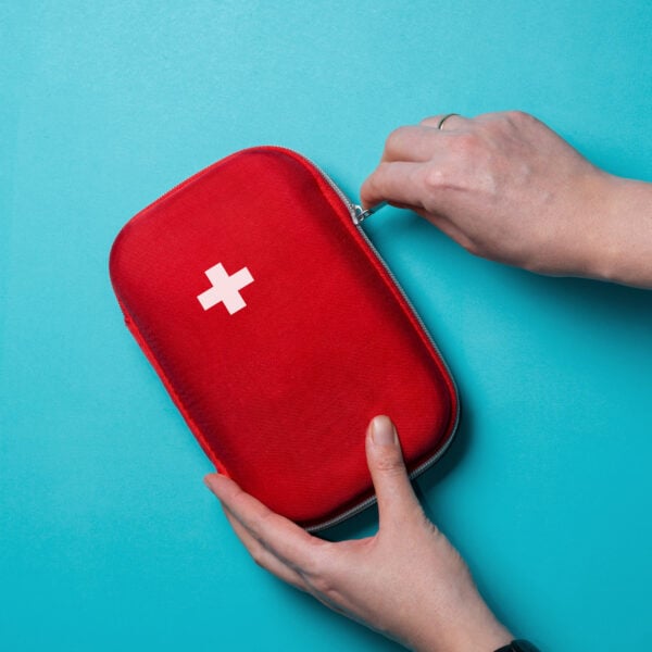 A person opens a red first aid kit with a white cross on the cover, set against a blue background—an essential step in learning how to build an emergency kit for food allergies.