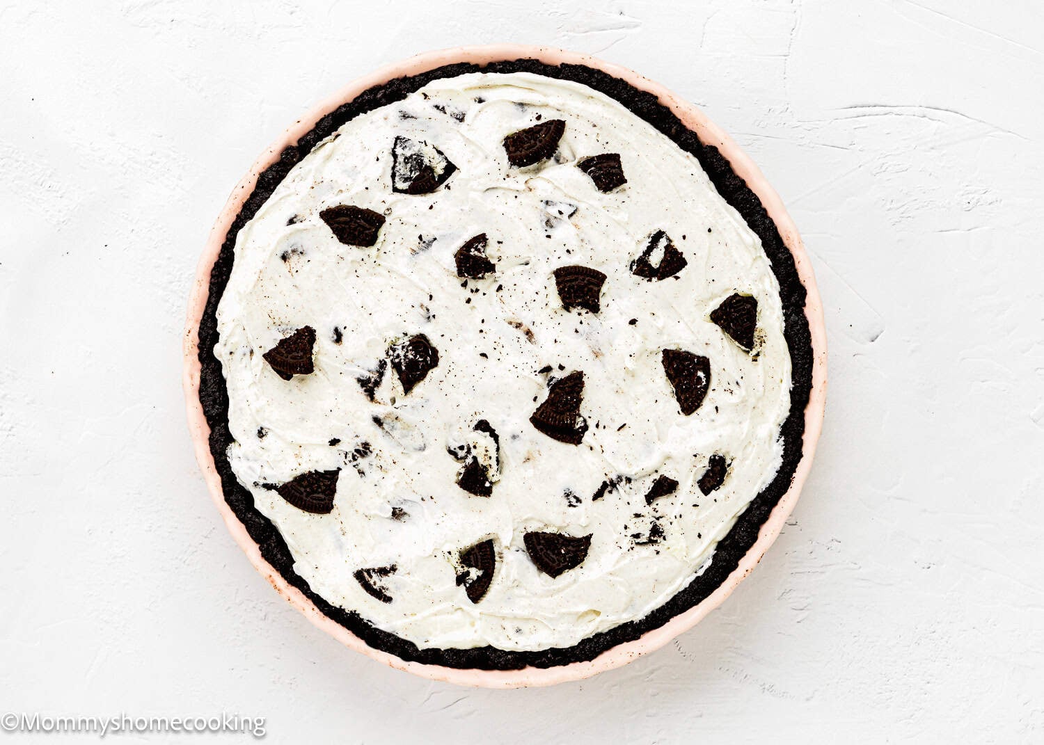A No Bake Oreo Cheesecake Pie with a dark cookie crust, topped with creamy white filling and chunks of chocolate cookies, displayed on a white background.