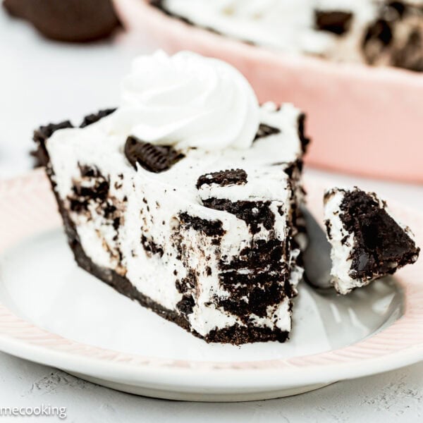 A slice of No Bake Oreo Cheesecake Pie with whipped topping sits on a plate, a forkful already taken.