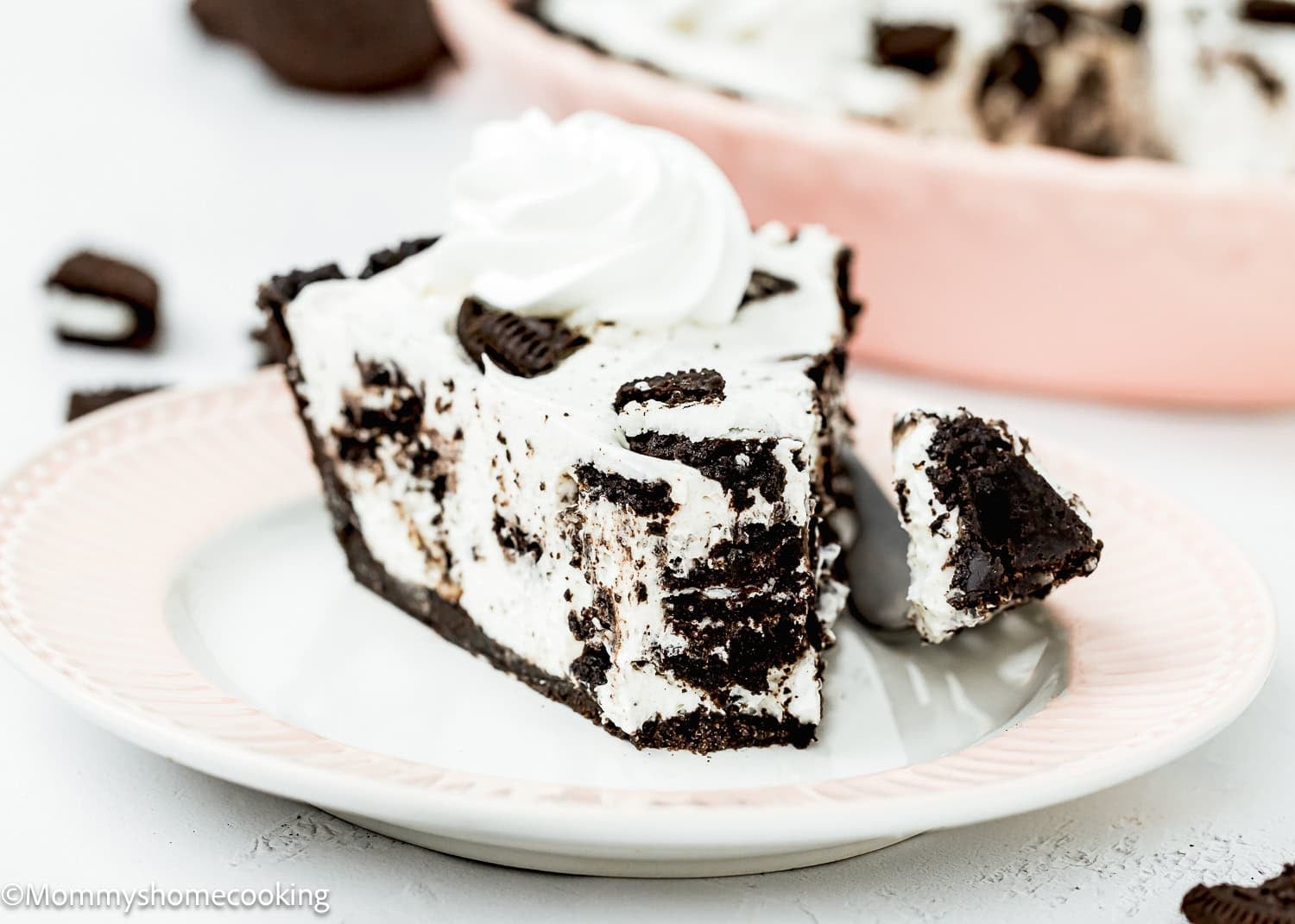 A slice of No Bake Oreo Cheesecake Pie with whipped topping sits on a plate, a forkful already taken.
