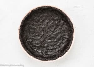 A round baking dish with a pressed, unbaked chocolate cookie crust on a white surface, perfect for making No Bake Oreo Cheesecake Pie.
