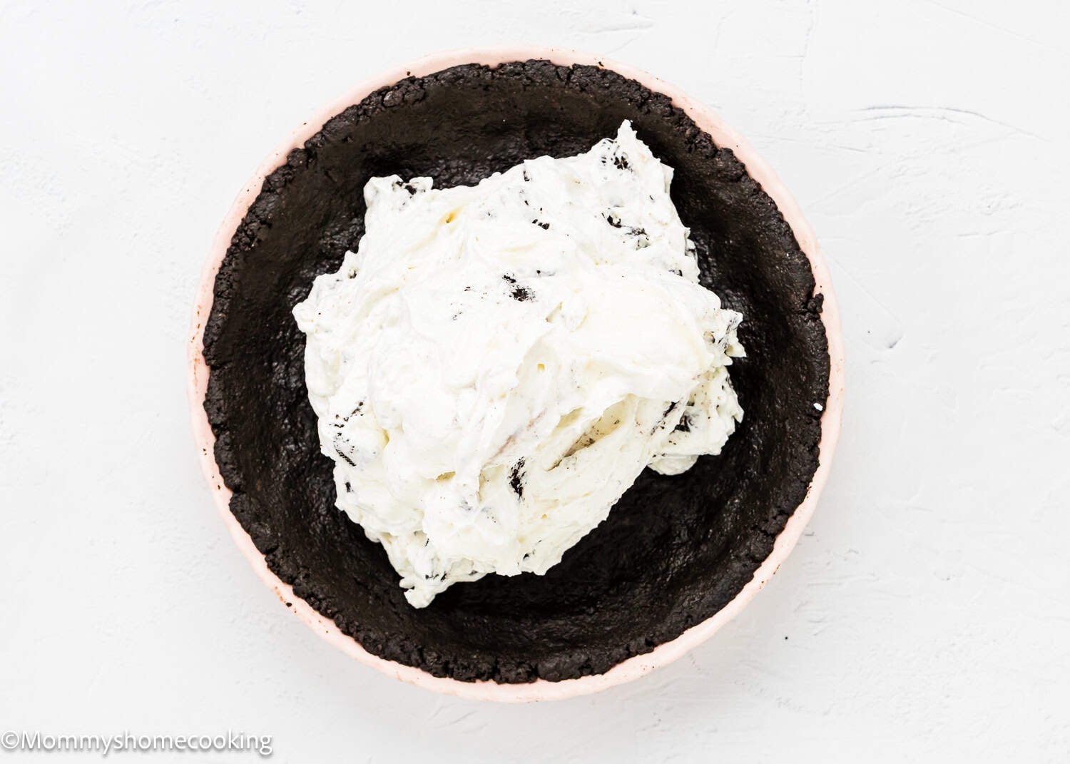 A pie crust made from crushed cookies is filled with a mound of whipped cream-based mixture, creating a delicious No Bake Oreo Cheesecake Pie on a white background.
