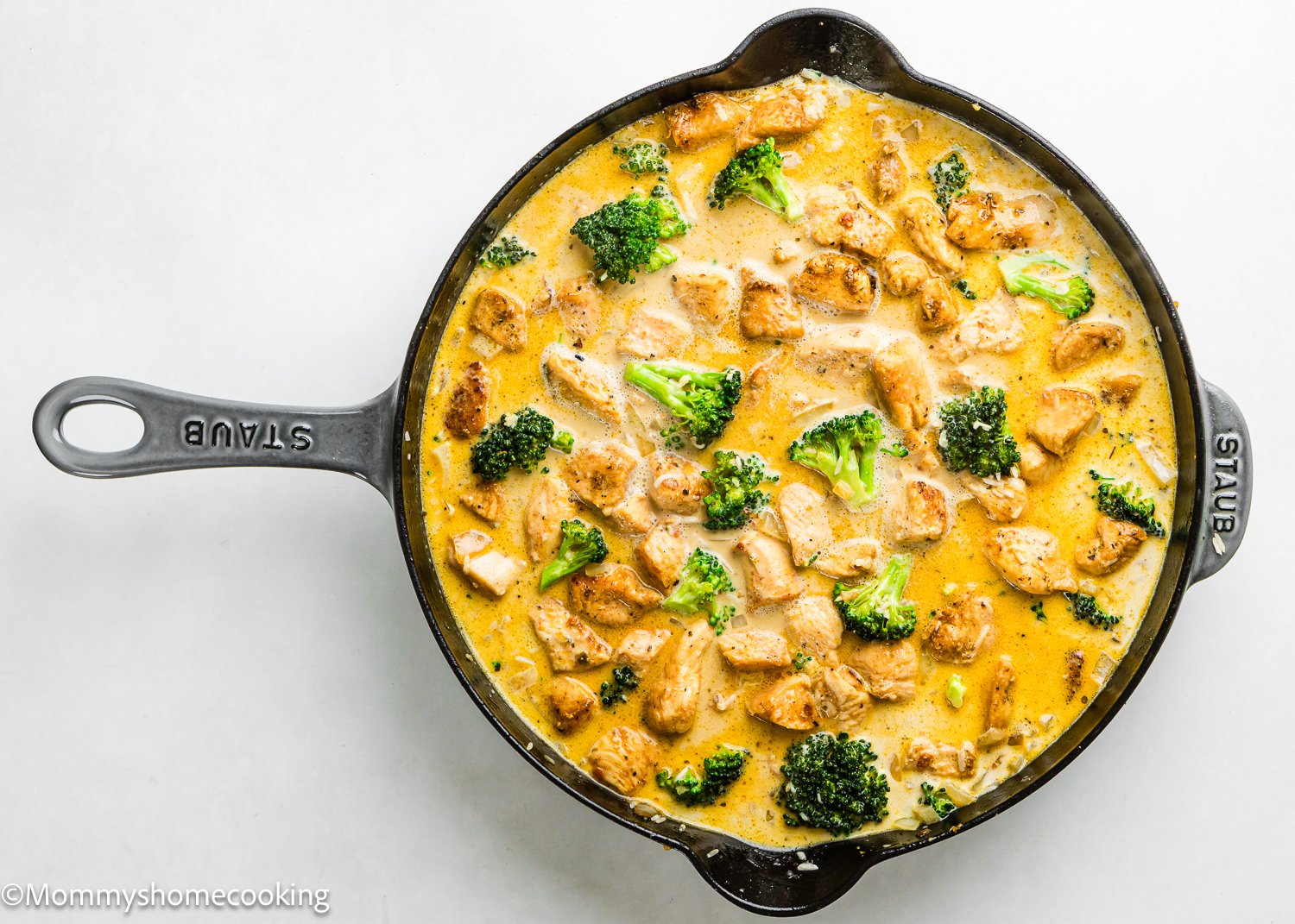A cast iron skillet filled with creamy One Pot Chicken Broccoli Rice Casserole in a yellow sauce, viewed from above on a white background.