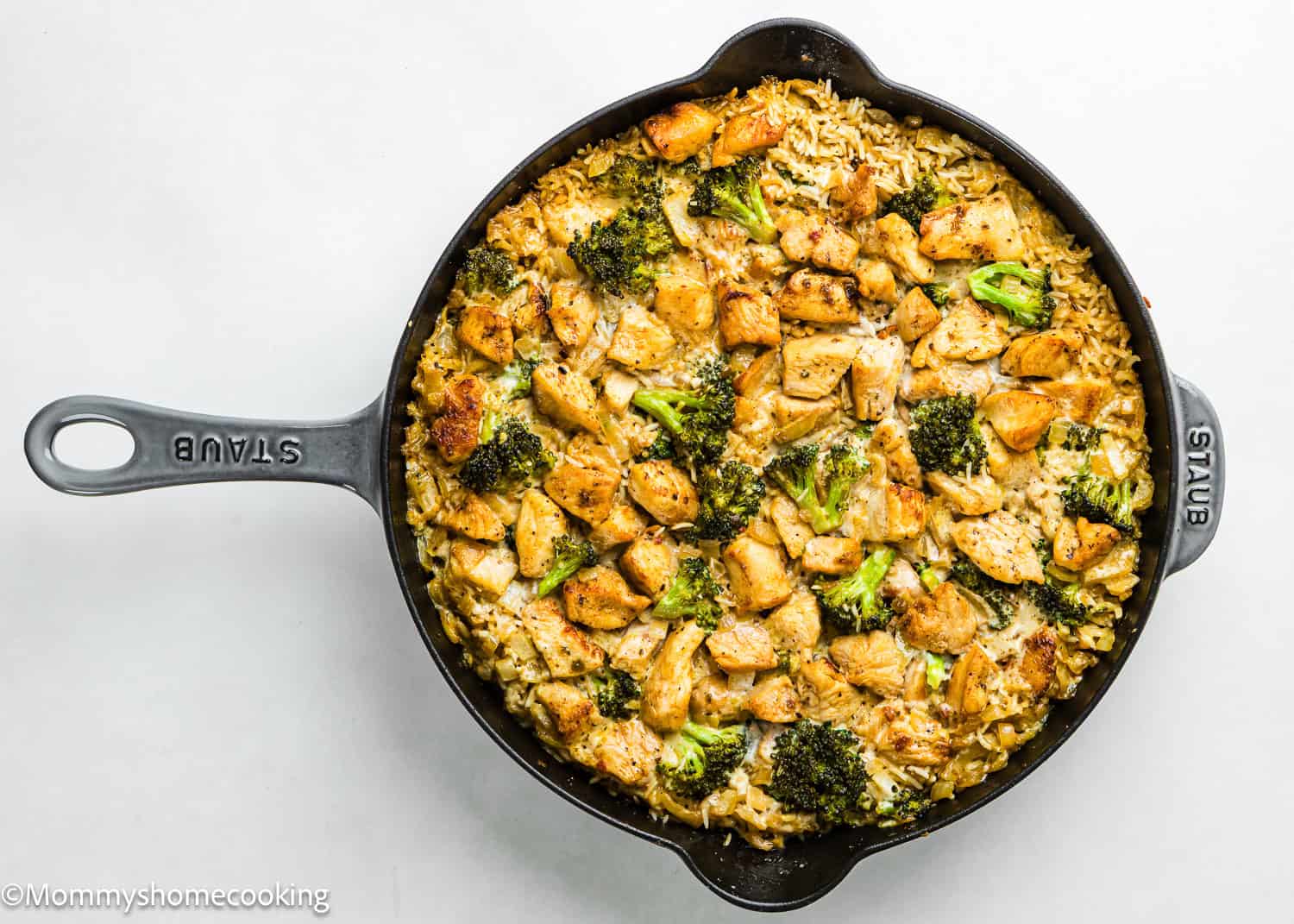 A skillet filled with One Pot Chicken Broccoli Rice Casserole, featuring cooked rice, diced chicken, and broccoli pieces on a white background.