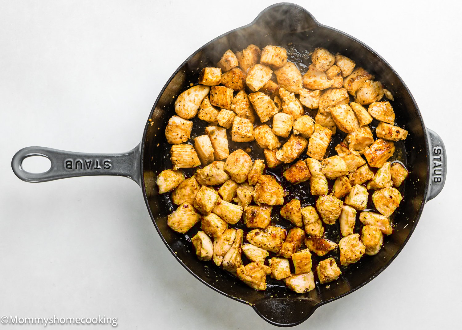 Cubed, seasoned chicken pieces are cooking in a black cast iron skillet, viewed from above—a delicious start for a One Pot Chicken Broccoli Rice Casserole.