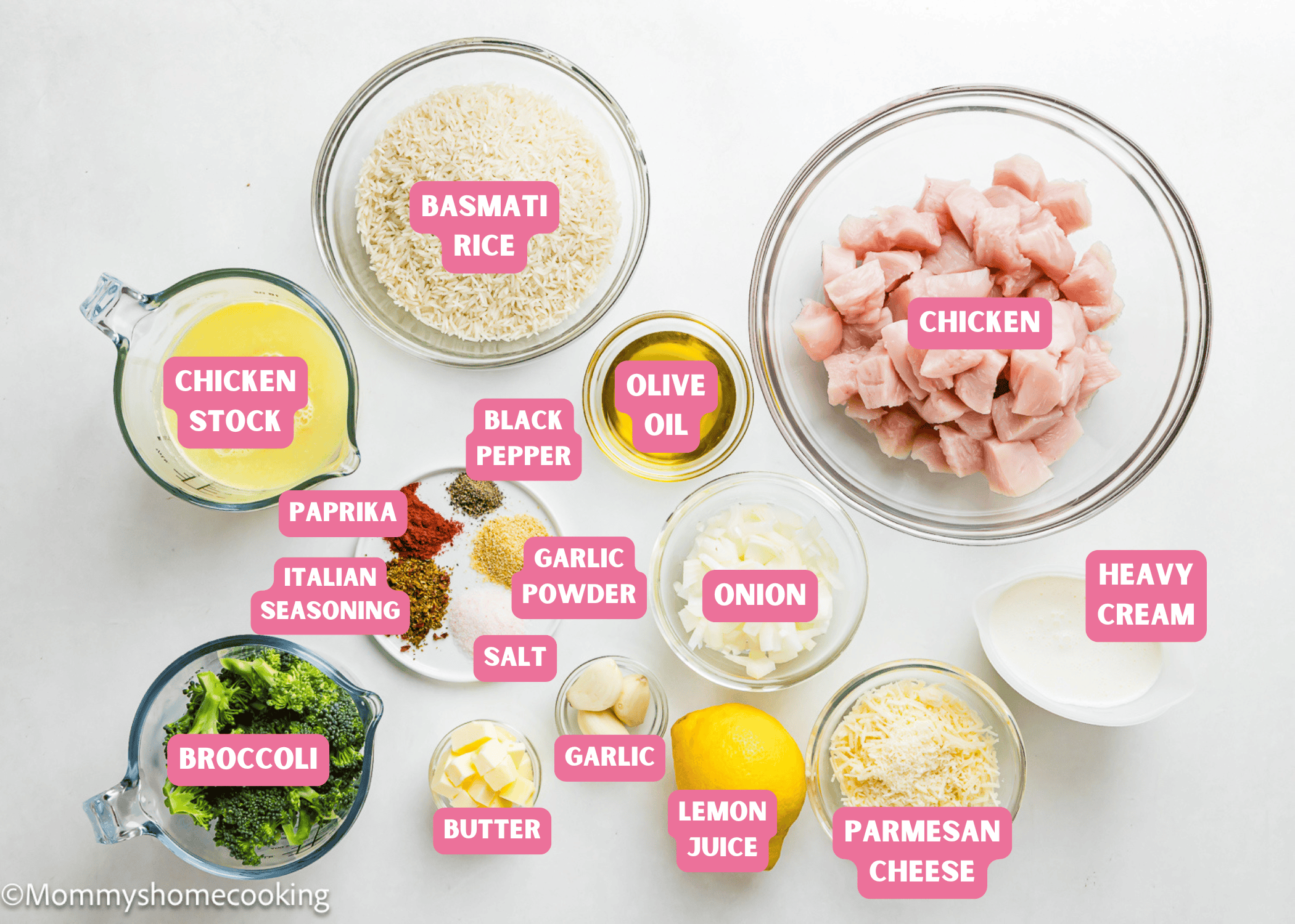 Overhead view of labeled ingredients for One Pot Chicken Broccoli Rice Casserole in bowls and cups, including chicken, basmati rice, broccoli, chicken stock, spices, olive oil, onion, garlic, butter, lemon juice, Parmesan, and heavy cream.