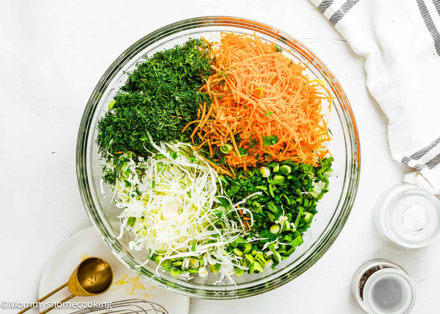 A glass bowl containing shredded carrots, chopped dill, sliced green onions, and shredded cabbage on a white surface—perfect for a Simple Cabbage Salad (No Mayo).