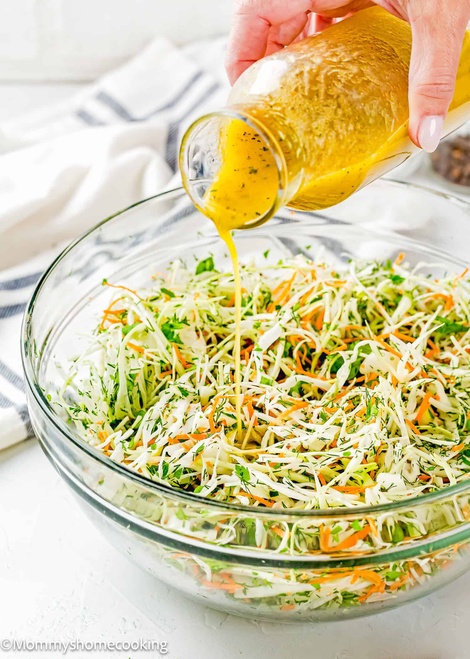 A hand pours yellow vinaigrette dressing onto a bowl of shredded cabbage, carrots, and herbs for a Simple Cabbage Salad (No Mayo).