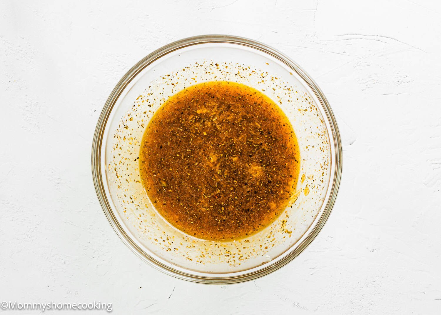 A clear glass bowl filled with a reddish-brown Simple Shrimp Marinade (Perfect for Grilling!) mixture sits on a white surface.