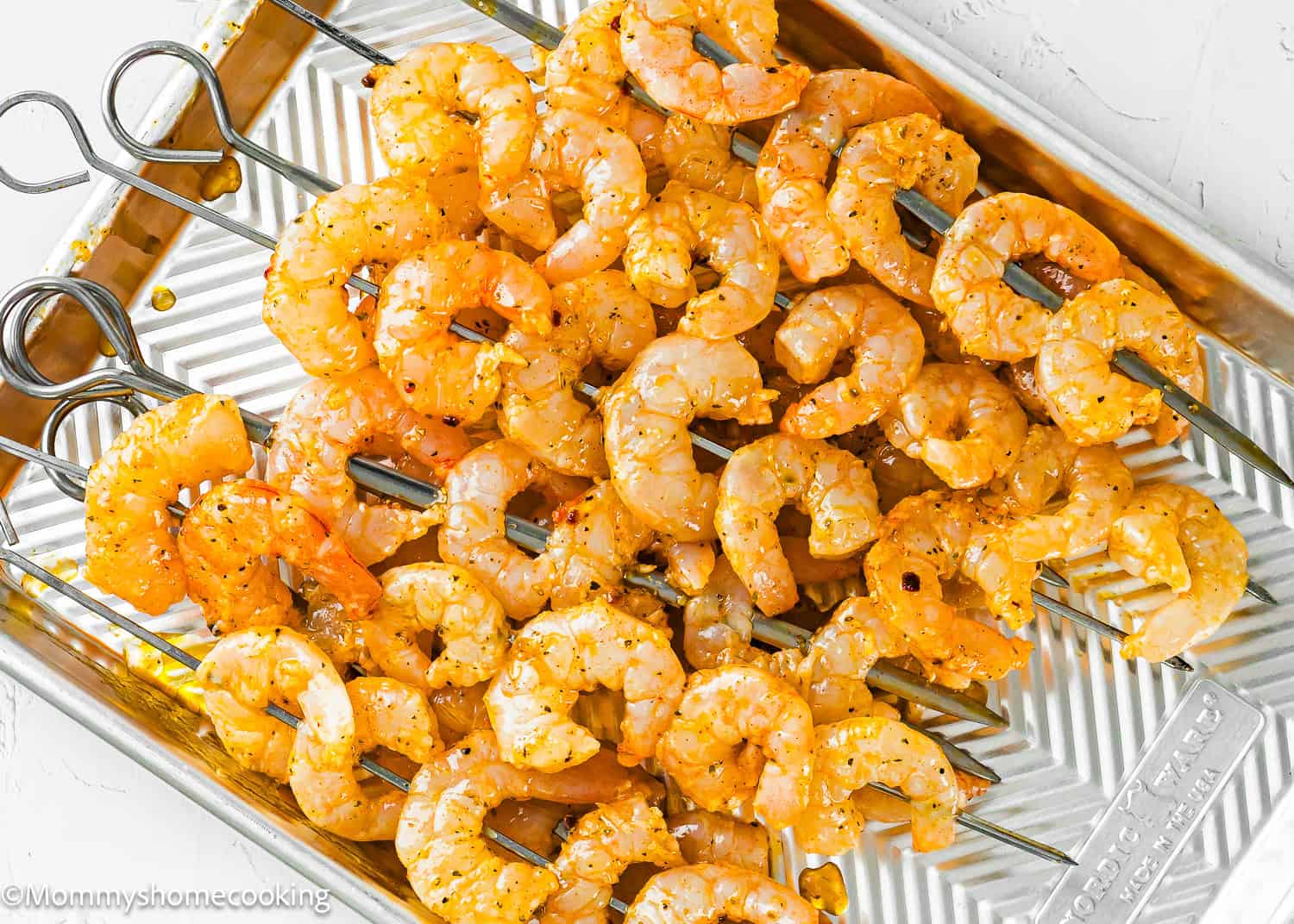 Metal skewers with seasoned raw shrimp, marinated to perfection, are arranged on a silver tray—ready for some flavorful shrimp grilling.