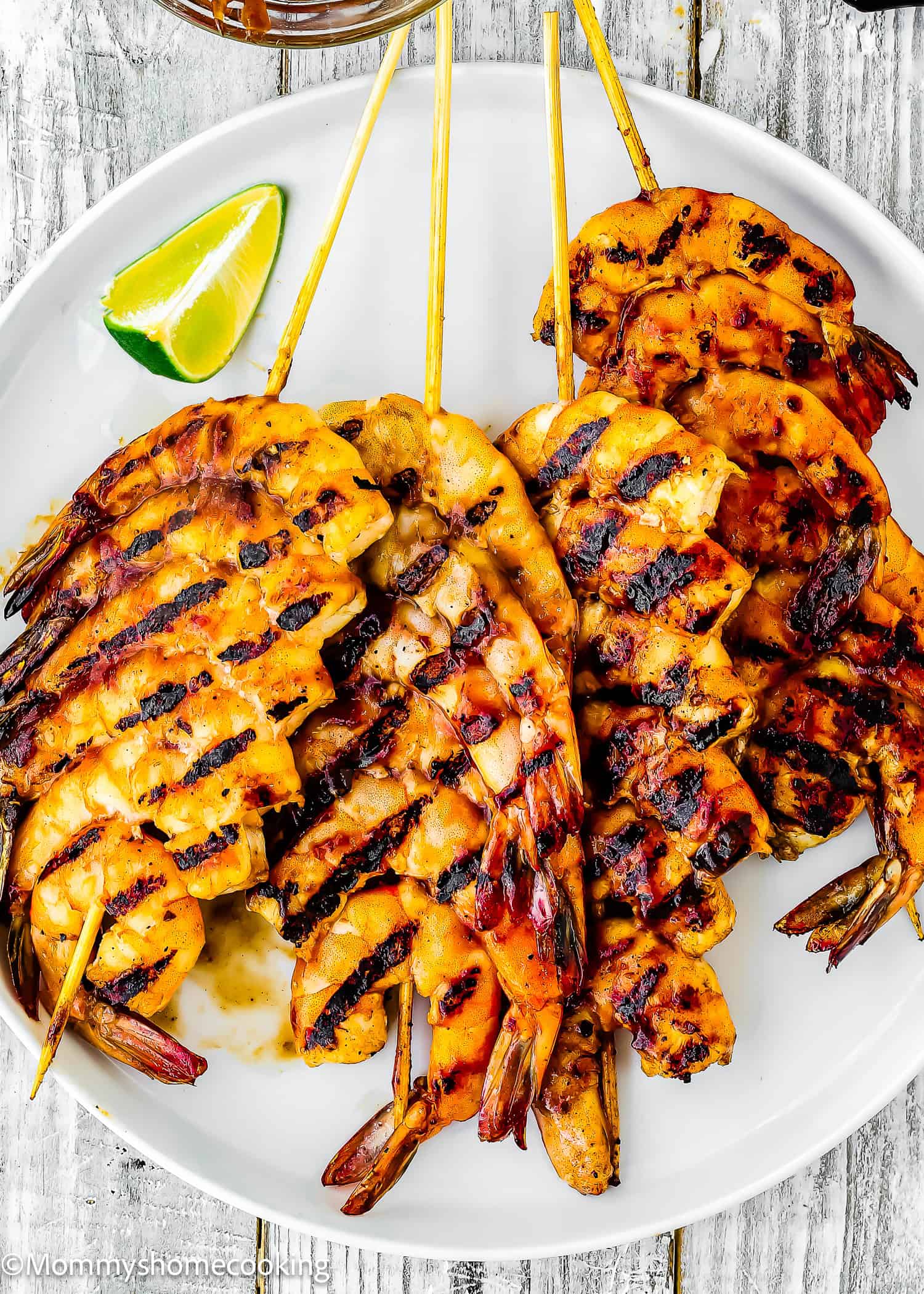 Super Easy Grilled Barbecue Shrimp skewers arranged on a white plate with grill marks, served with a wedge of lime.